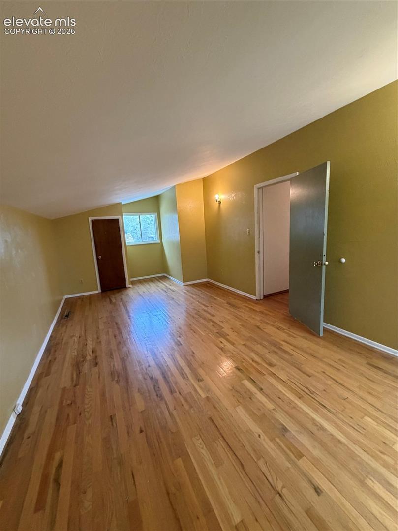 Room featuring wood-finish flooring, vaulted ceilings, and a window