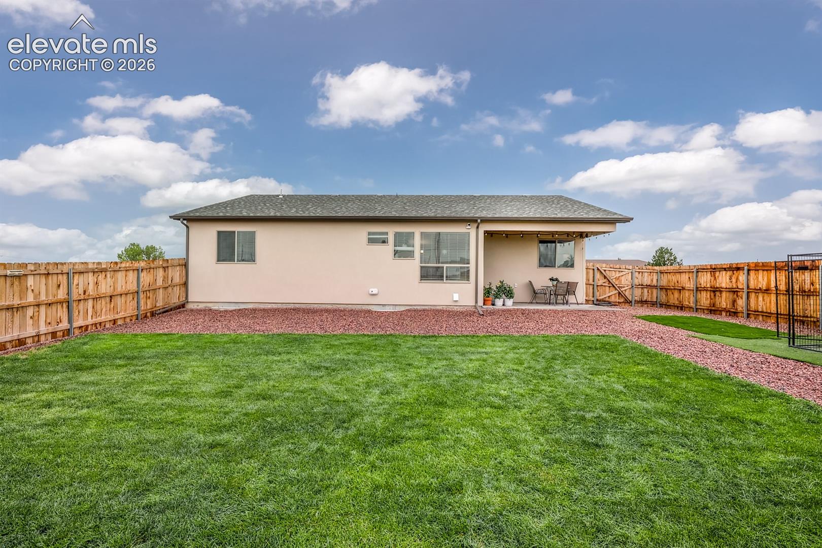 Backyard featuring a manicured lawn, red decorative rock landscaping, a covered patio, and wood privacy fencing