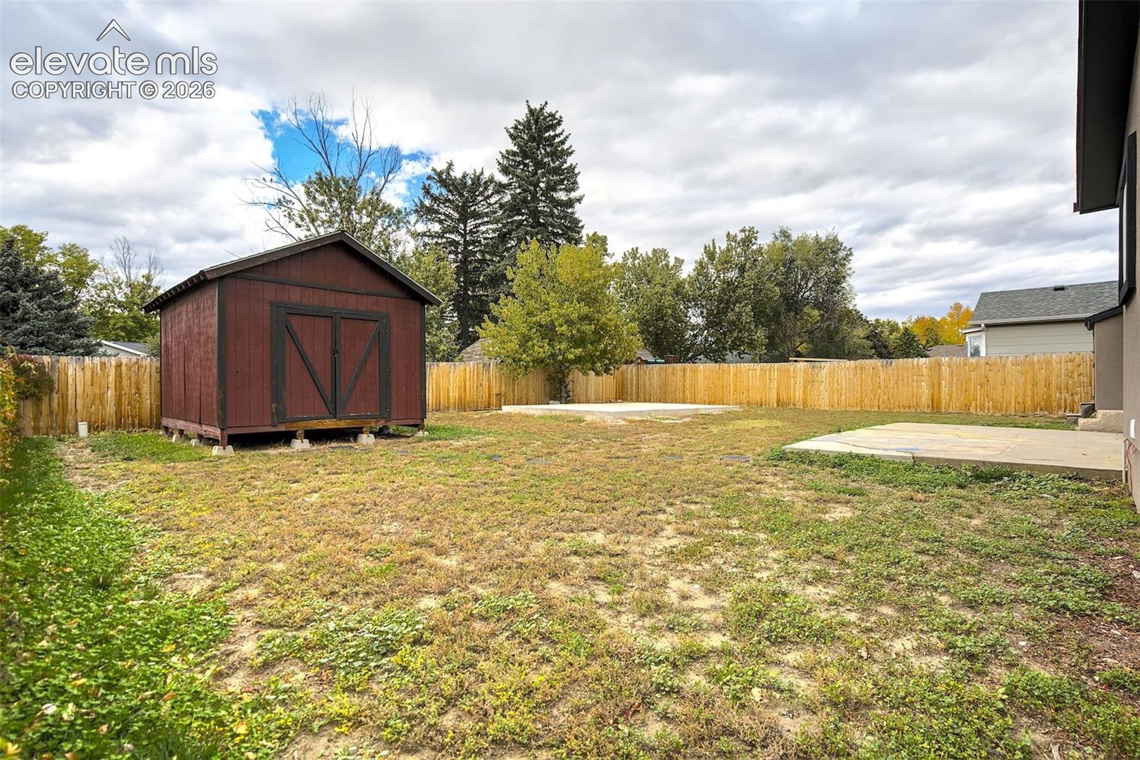Backyard featuring a wood-panel privacy fence, a detached storage shed, and a concrete patio