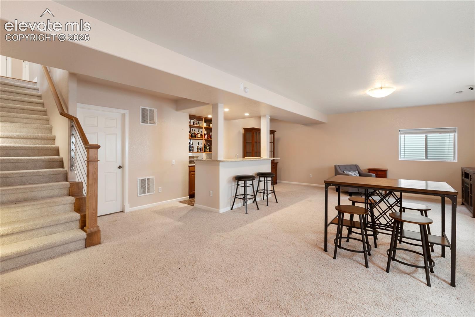 Carpeted staircase with wood and metal railing, integrated wet bar with built-in cabinetry, recessed lighting, and a window with blinds