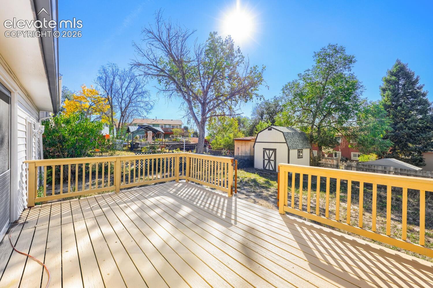 Expansive outdoor deck with natural wood railing, white siding, and a detached storage shed