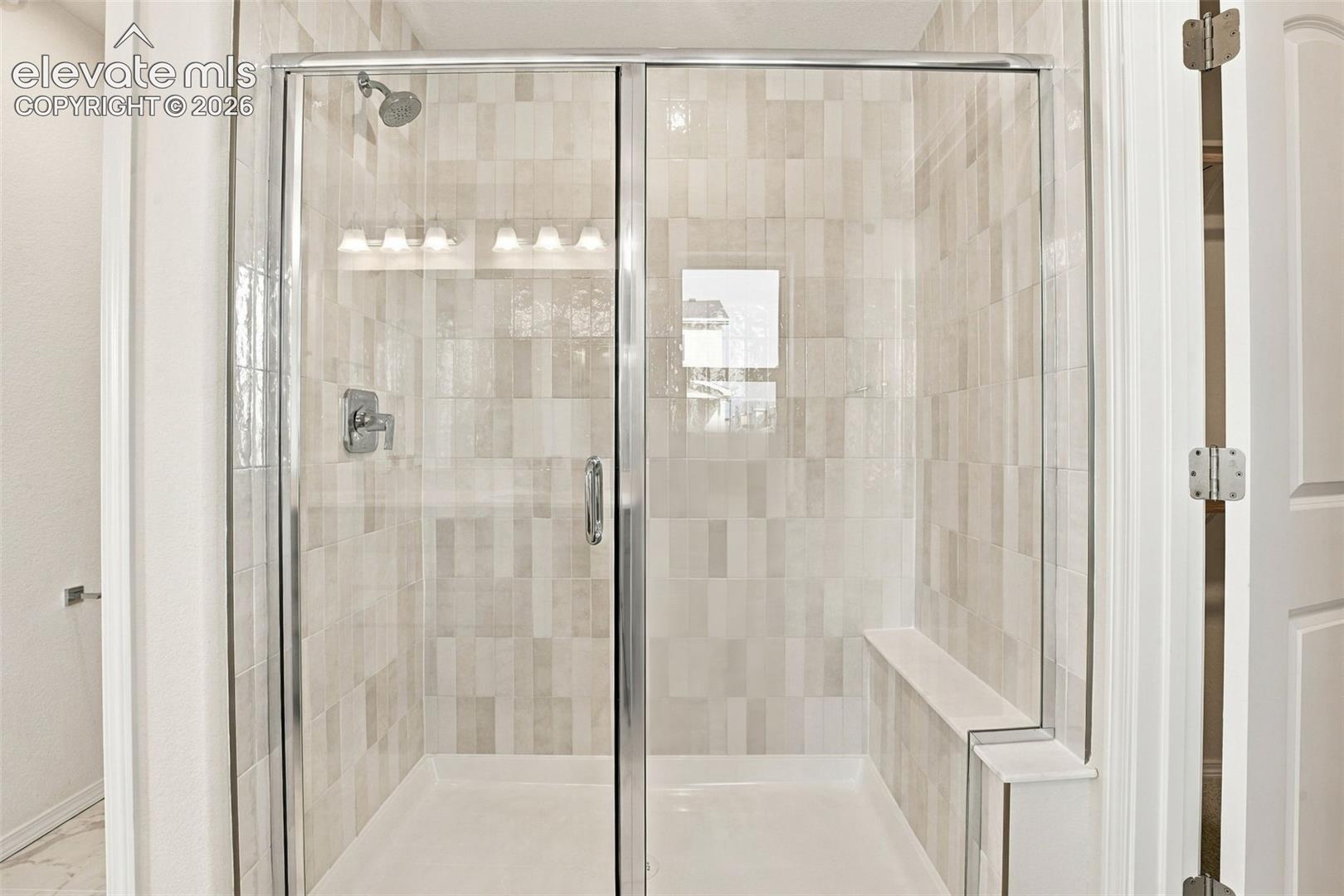 Walk-in shower featuring a chrome-framed glass enclosure, built-in bench seating, stacked-tile wall surfacing, and chrome shower fixtures
