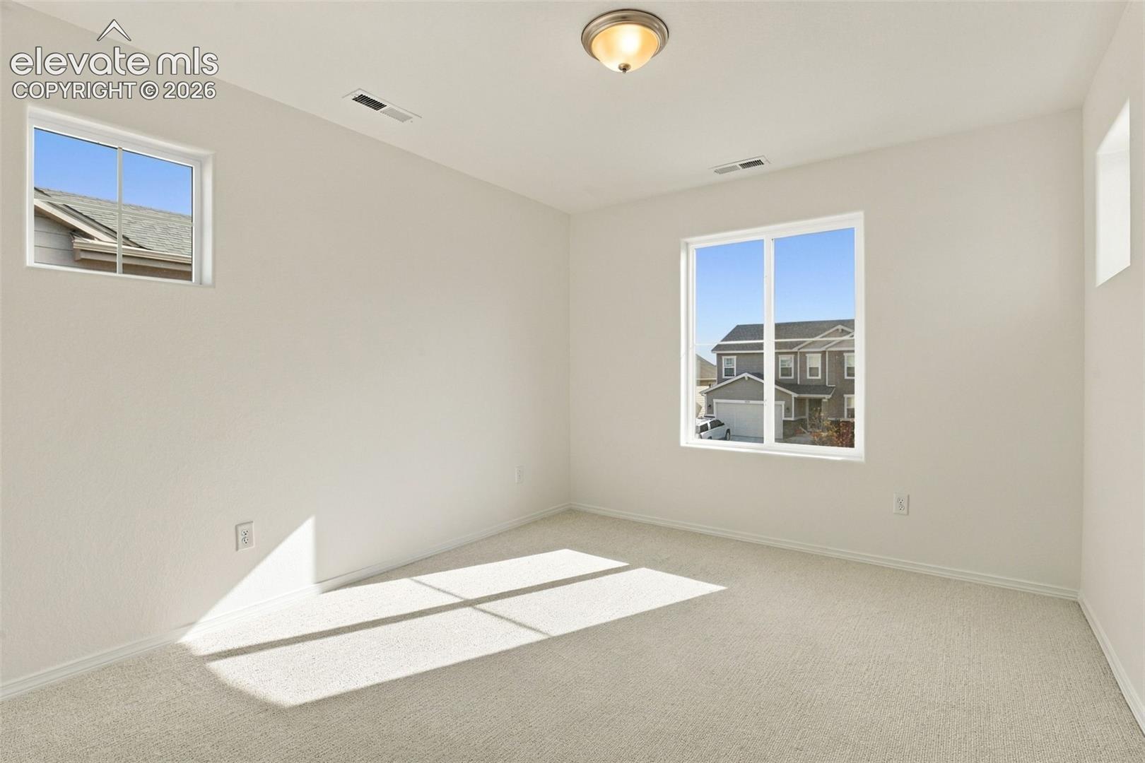 Neutral-toned interior space featuring light-colored wall-to-wall carpeting, multiple windows providing natural light, and a flush-mount ceiling fixture
