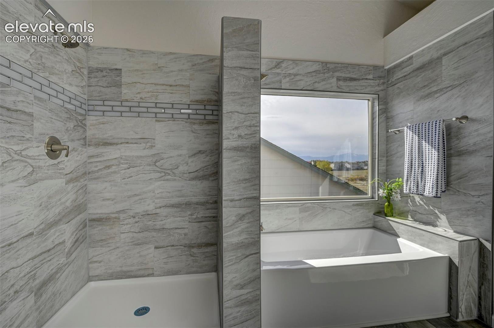 Walk-in shower with stone-tile surround, tile inlay accent, built-in soaking tub, and window with exterior mountain scenery