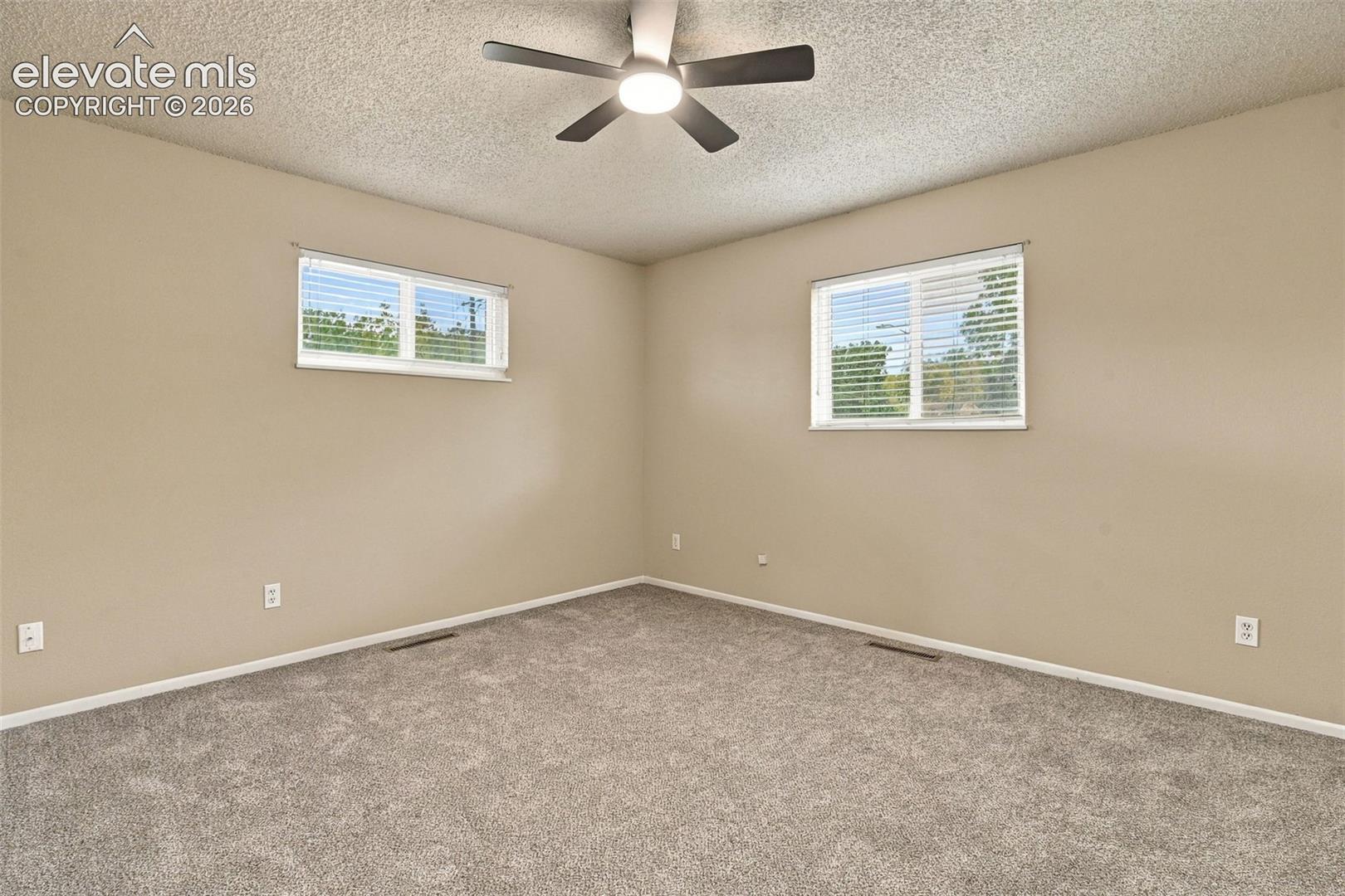 Neutral-toned room featuring neutral-toned carpeting, two windows with horizontal blinds, and a central ceiling fan with integrated lighting