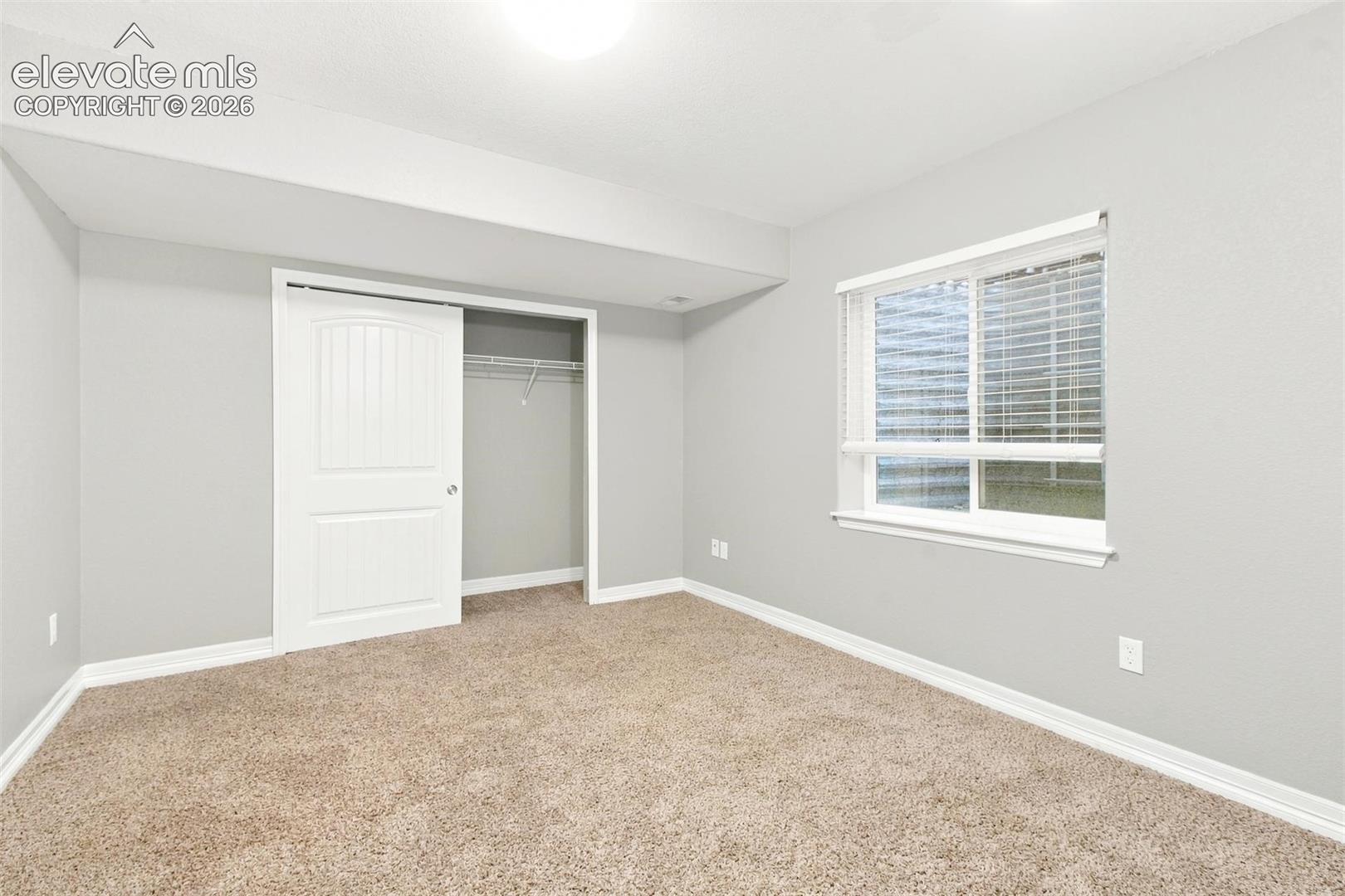 Neutral-toned interior featuring wall-to-wall carpeting, a sliding window with horizontal blinds, and a built-in closet with a paneled door