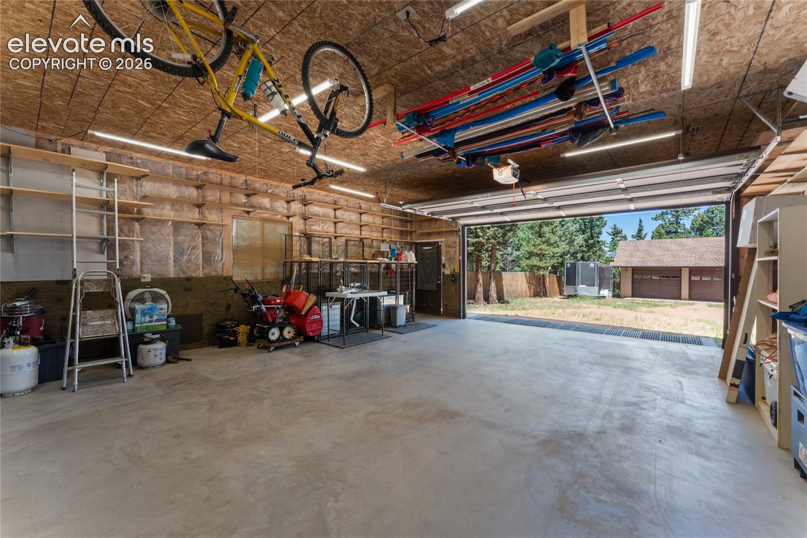 Spacious two-car garage with overhead storage, exposed wood-finish ceiling, and concrete flooring