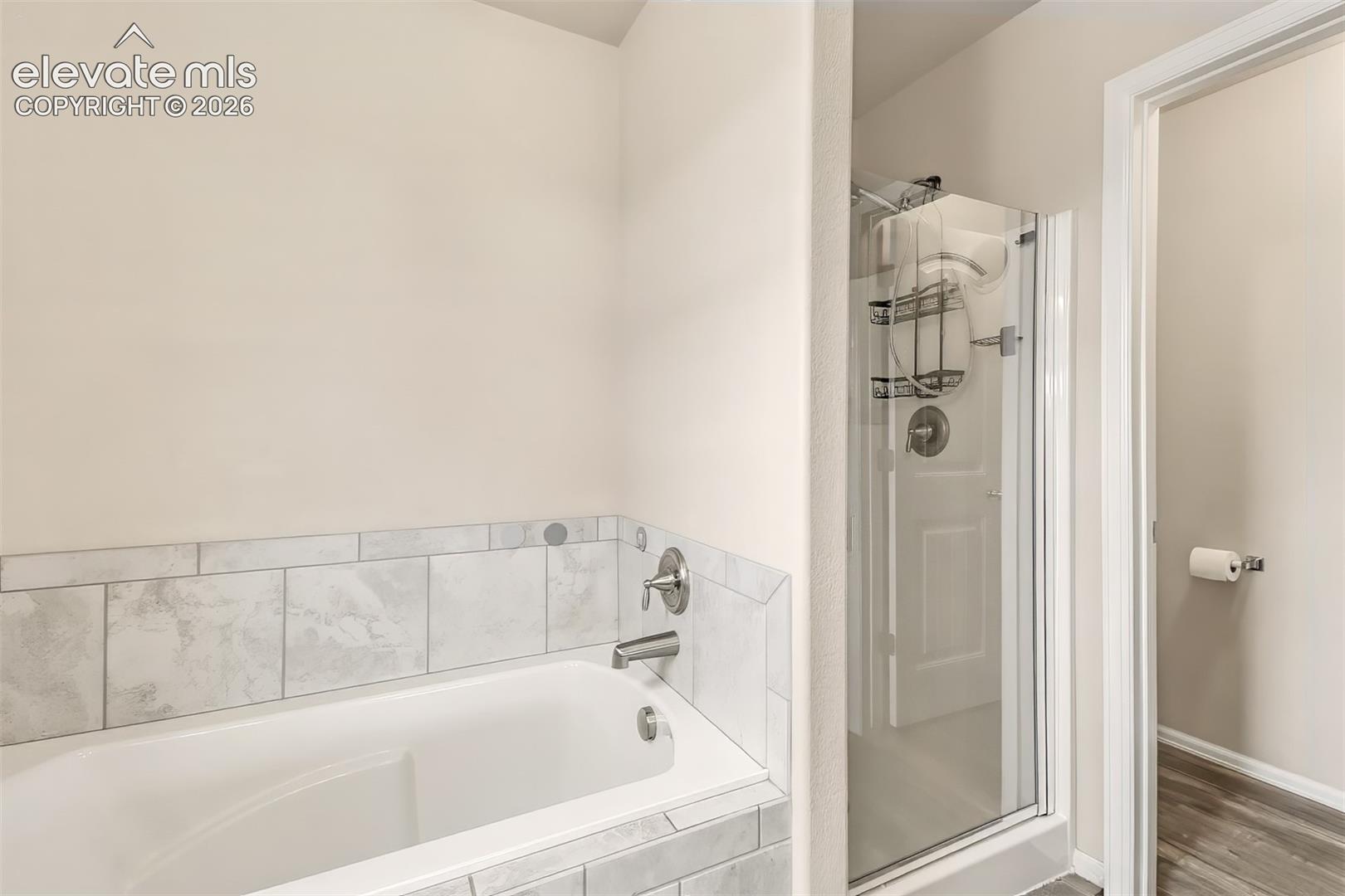 Soaking tub with a tile surround and chrome hardware, featuring a glass-enclosed shower stall