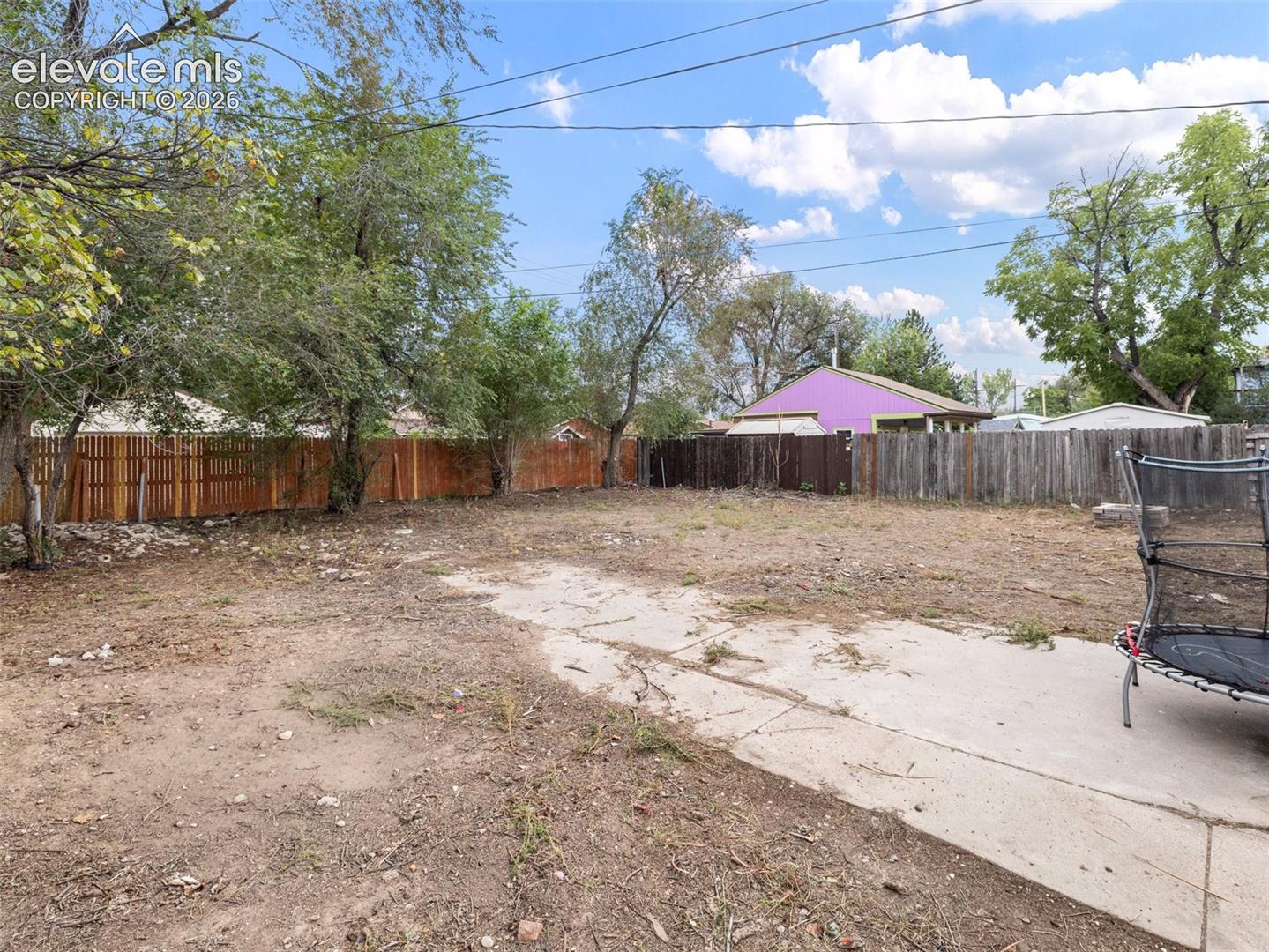 Spacious outdoor area featuring a concrete patio, perimeter fencing, and mature trees