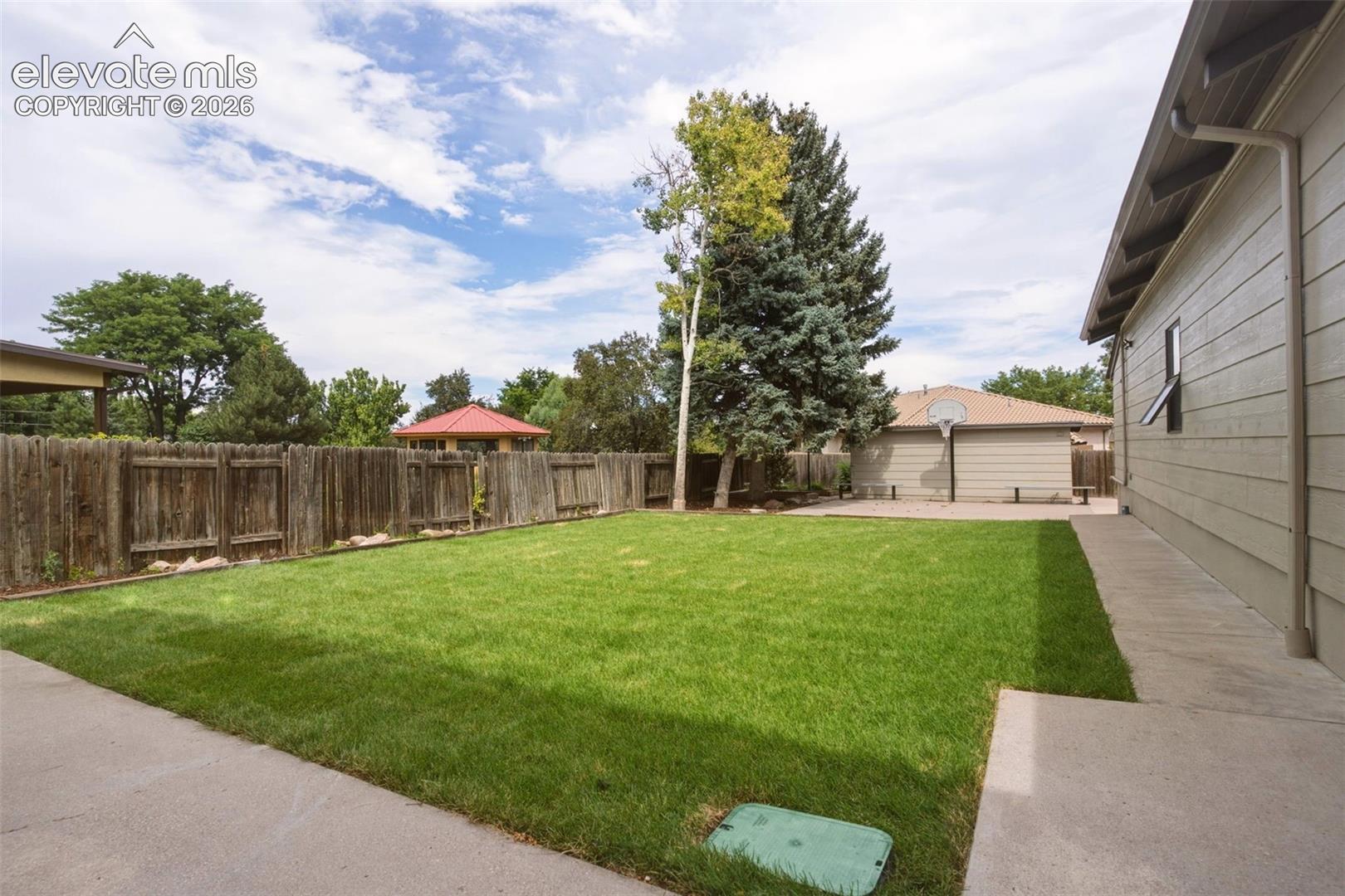 Expansive green lawn, mature trees, wood privacy fencing, and concrete pathway