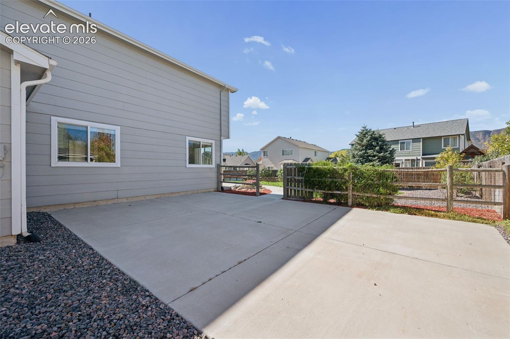 Concrete patio, horizontal lap siding, post-and-rail fencing, rock landscaping, and mountain backdrop