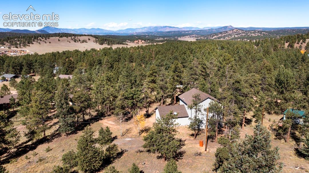 Multi-level residence featuring a pitched roof, situated on a heavily wooded lot with prominent mountain scenery