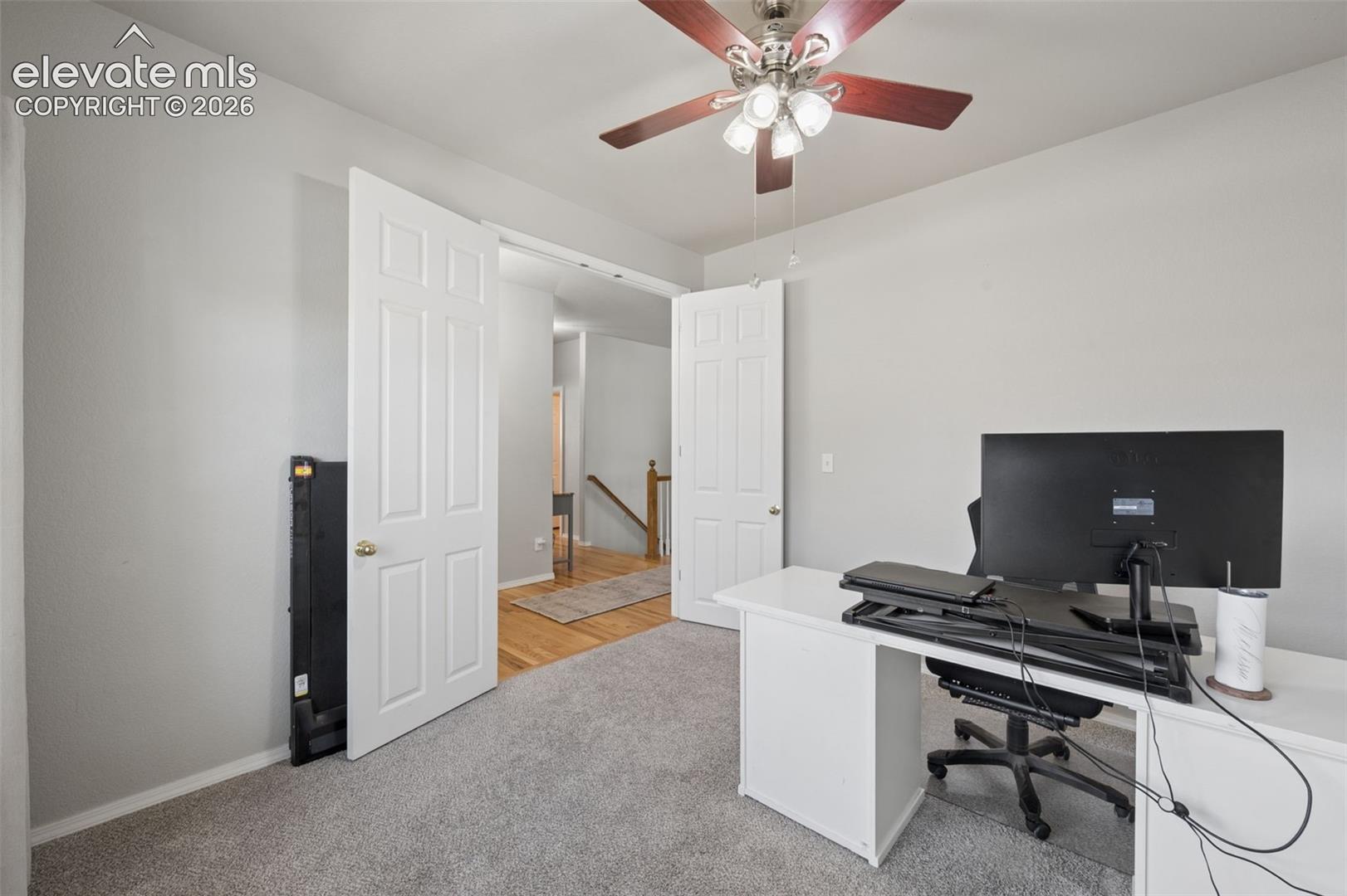 Neutral-toned interior space featuring wall-to-wall carpeting, a multi-light ceiling fan with wood-finish blades, and double six-panel interior doors