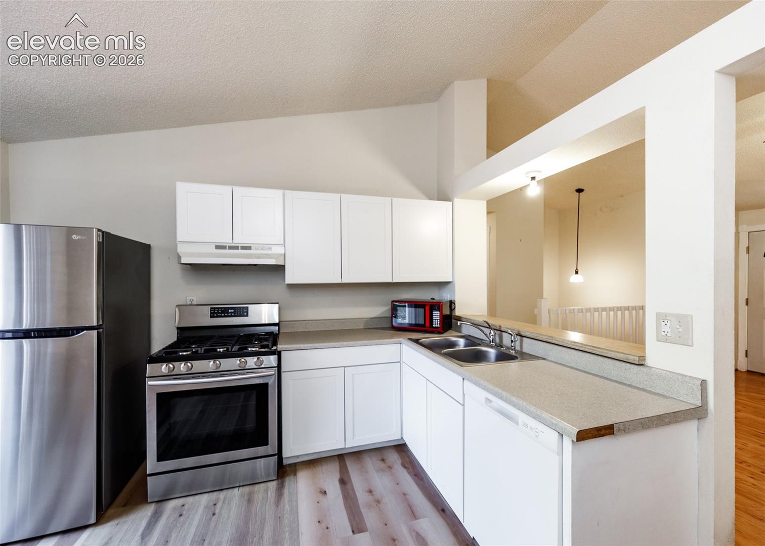 Kitchen featuring white shaker-style cabinetry, stainless steel gas range, stainless steel refrigerator, neutral solid-surface countertops, and wood-finish flooring