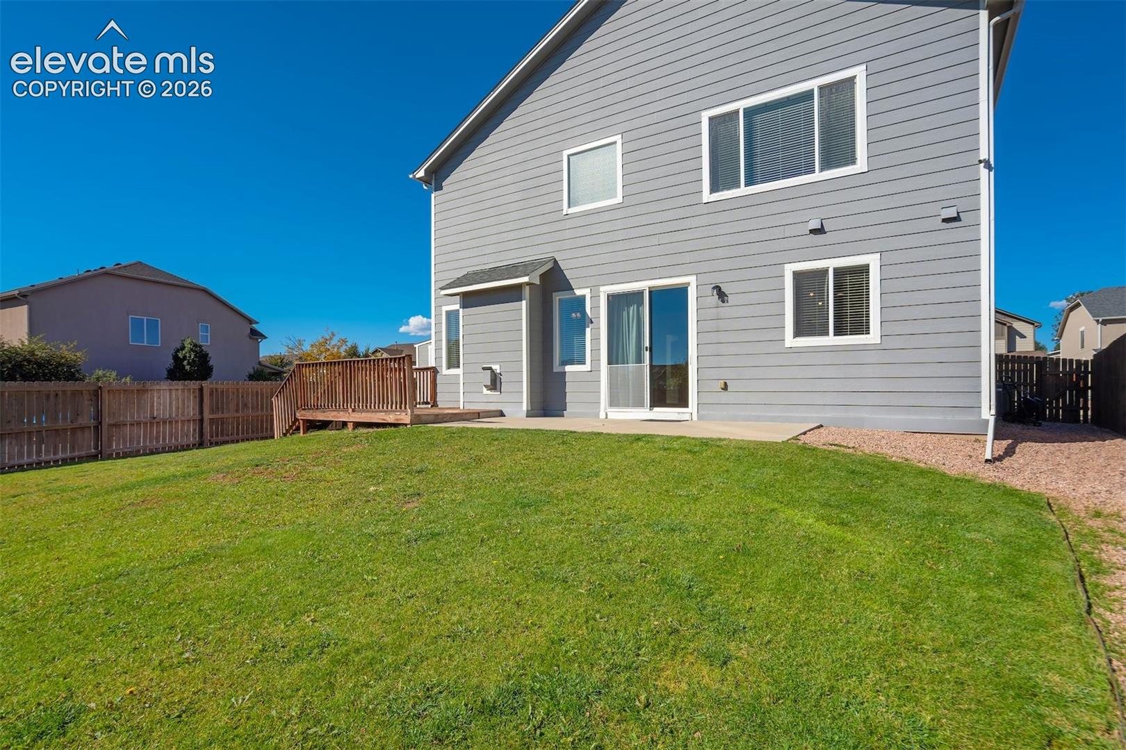 Expansive green lawn with a wood privacy fence, concrete patio, and a wood deck