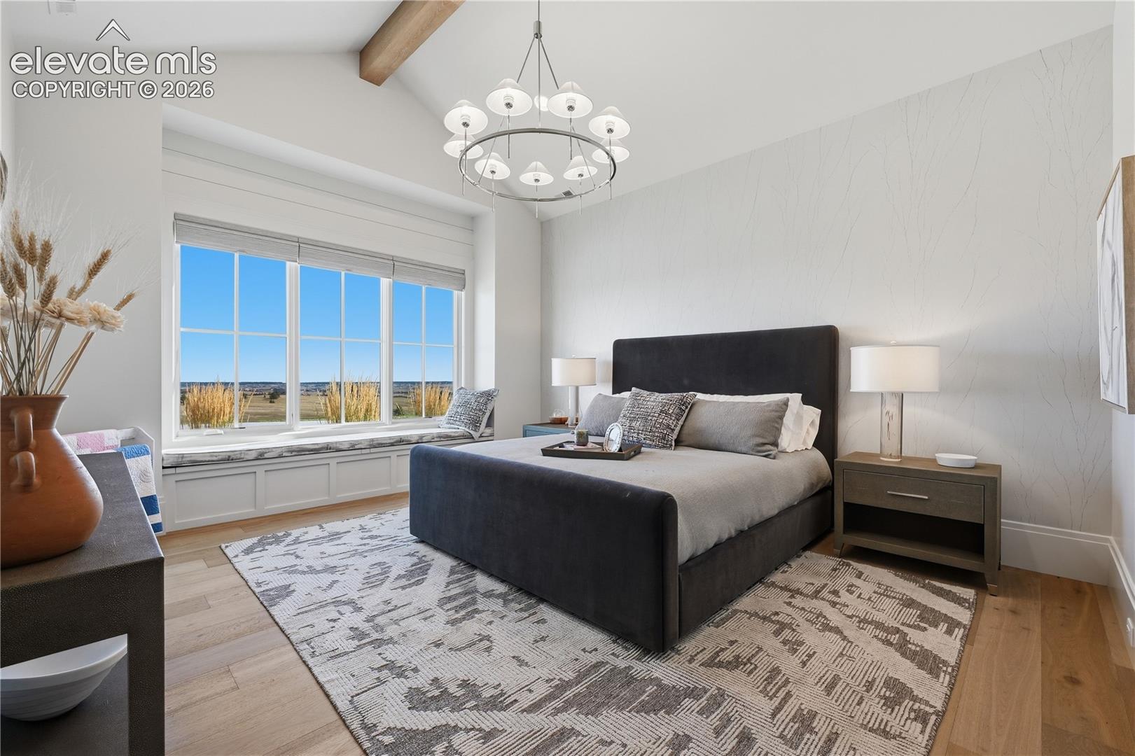 Vaulted ceiling with exposed wood beam, large multi-pane window with built-in bench seating, chandelier lighting, and wide-plank wood-finish flooring