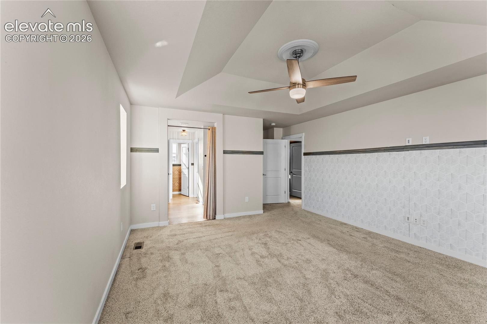 Tray ceiling featuring a central ceiling fan with integrated lighting, wall paneling with decorative trim, and neutral wall-to-wall carpeting