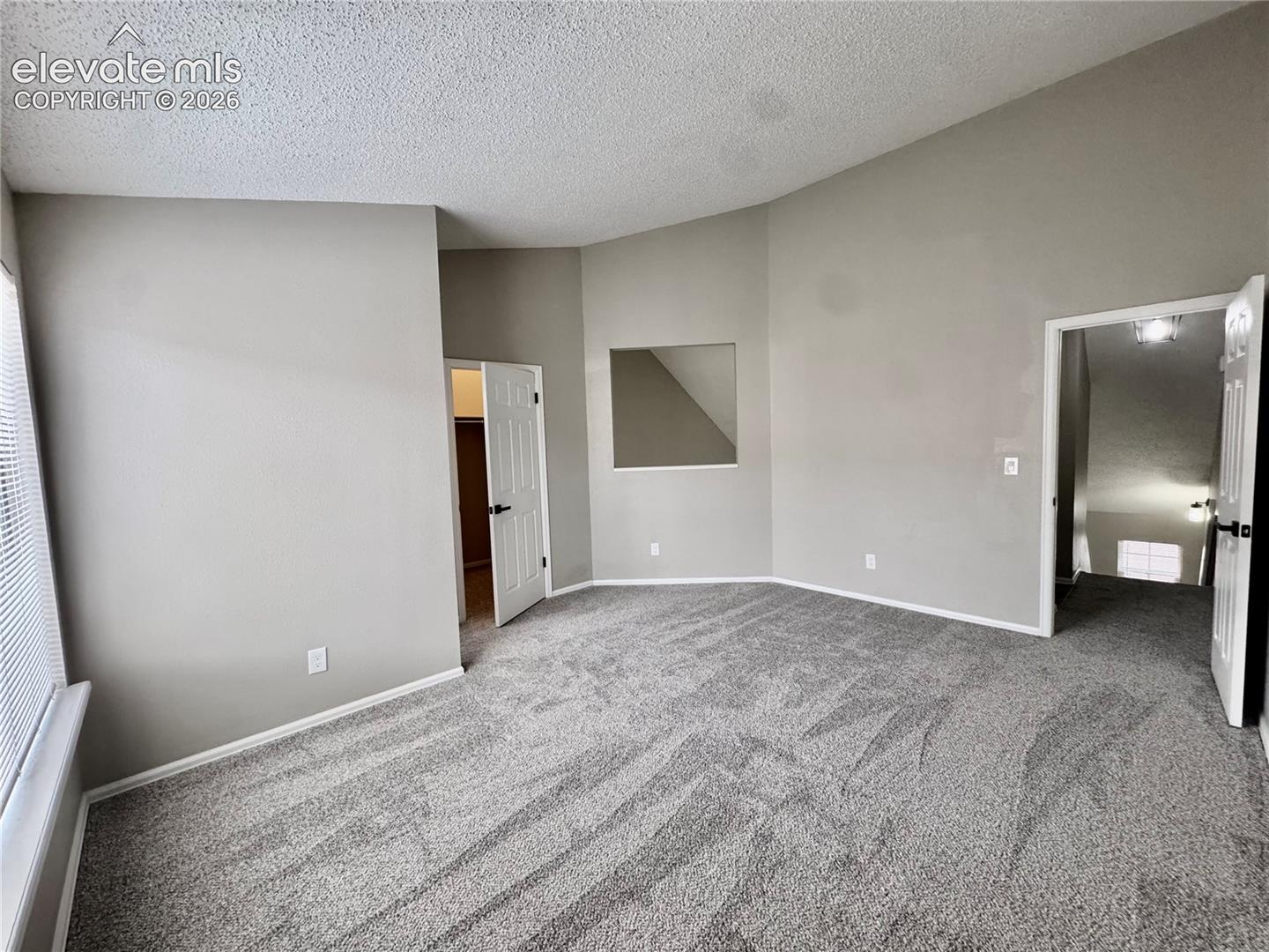 Vaulted ceiling, neutral wall paint, gray carpeting, white trim, and a window opening