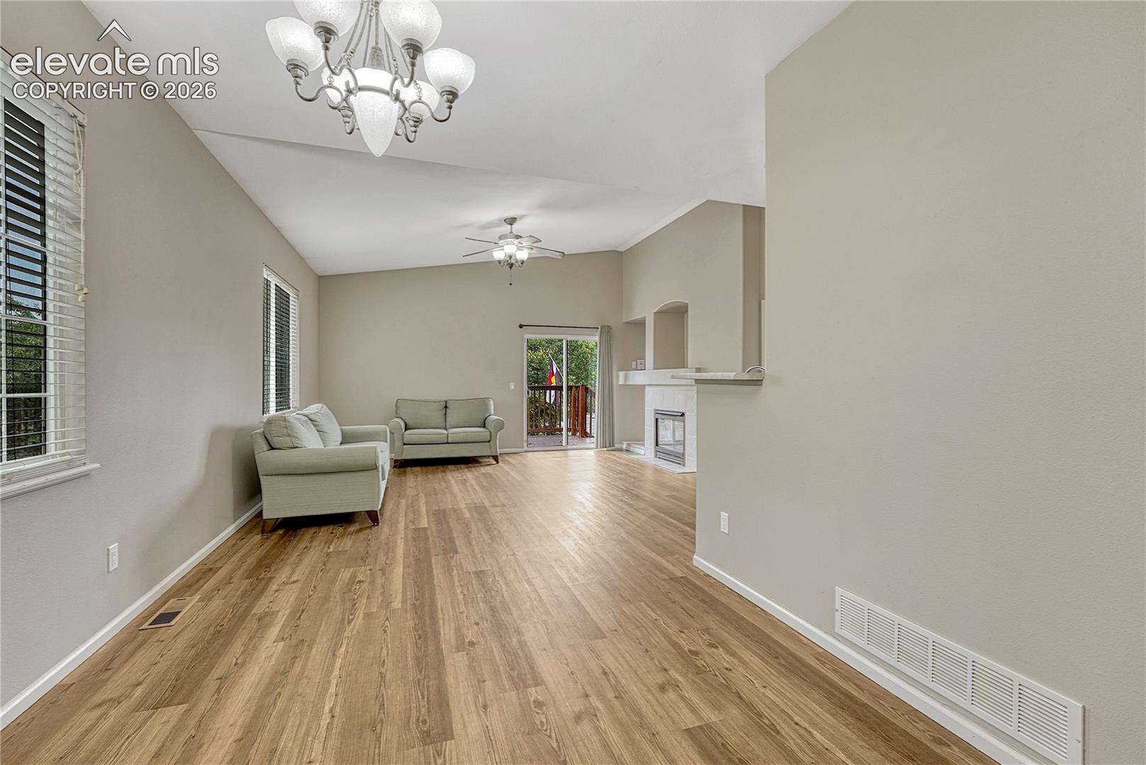 Vaulted ceilings, wood-finish flooring, multi-arm chandelier, ceiling fan, and fireplace with recessed niche
