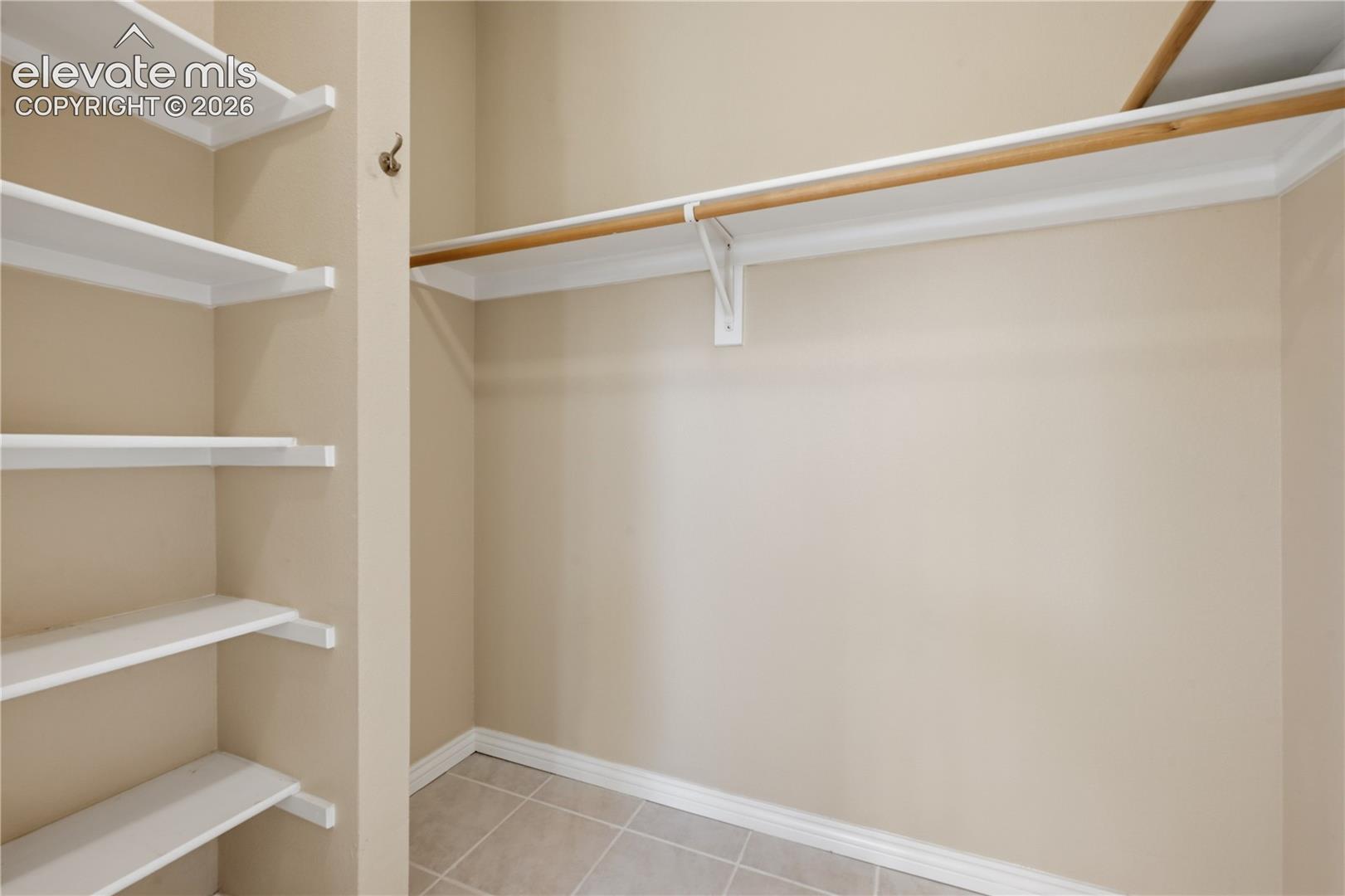 Storage space featuring built-in shelving and a mounted hanging rod with neutral tile flooring
