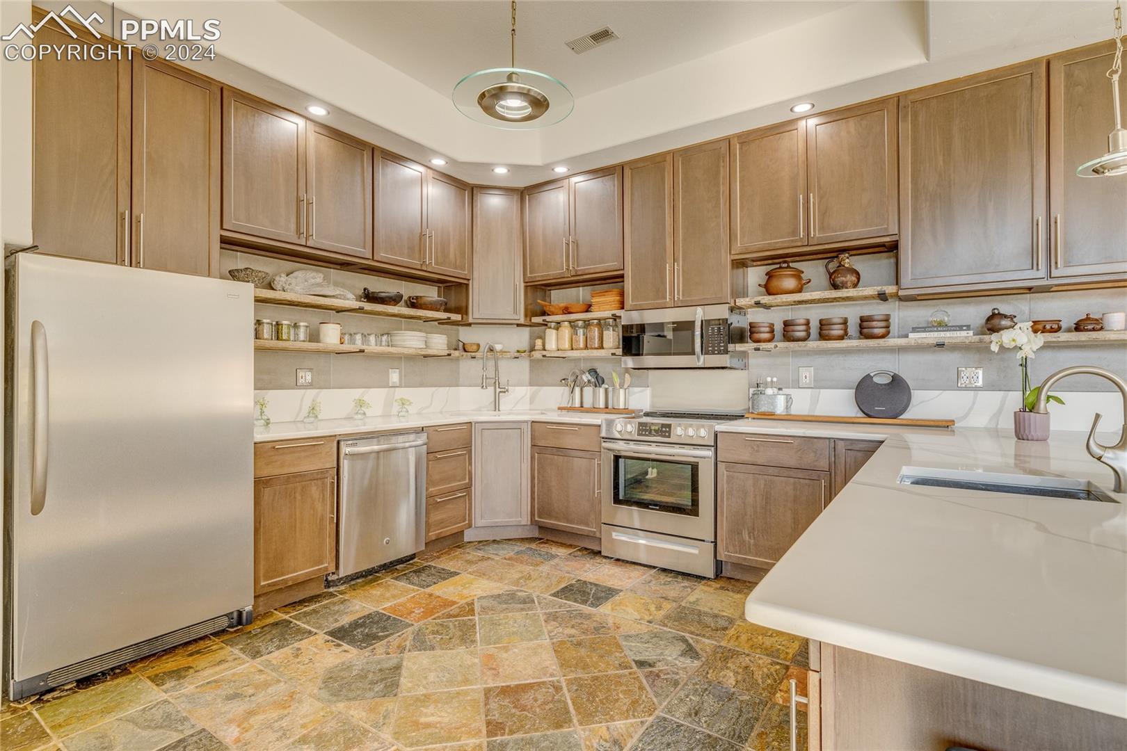 Kitchen with pendant lighting, appliances with stainless steel finishes, tile flooring, a raised ceiling, and sink