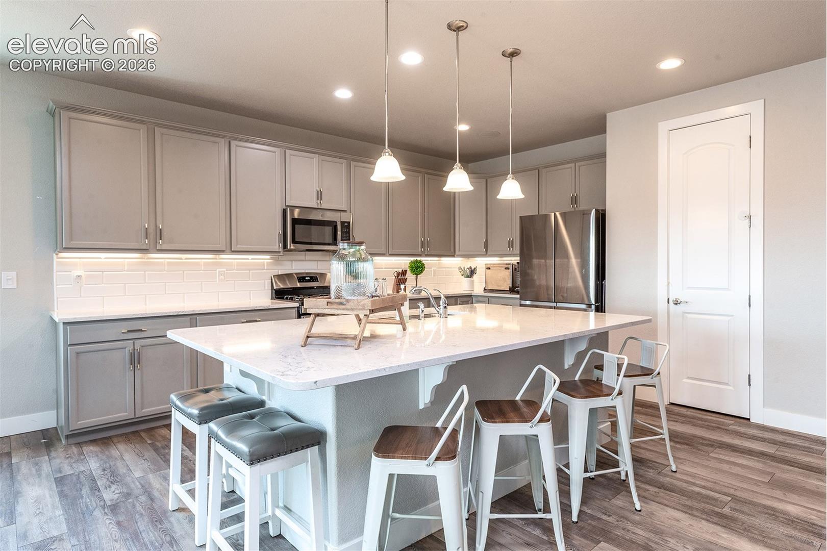 Kitchen featuring gray cabinetry, stainless steel appliances, a white subway tile backsplash, and a large central island with a light-colored countertop