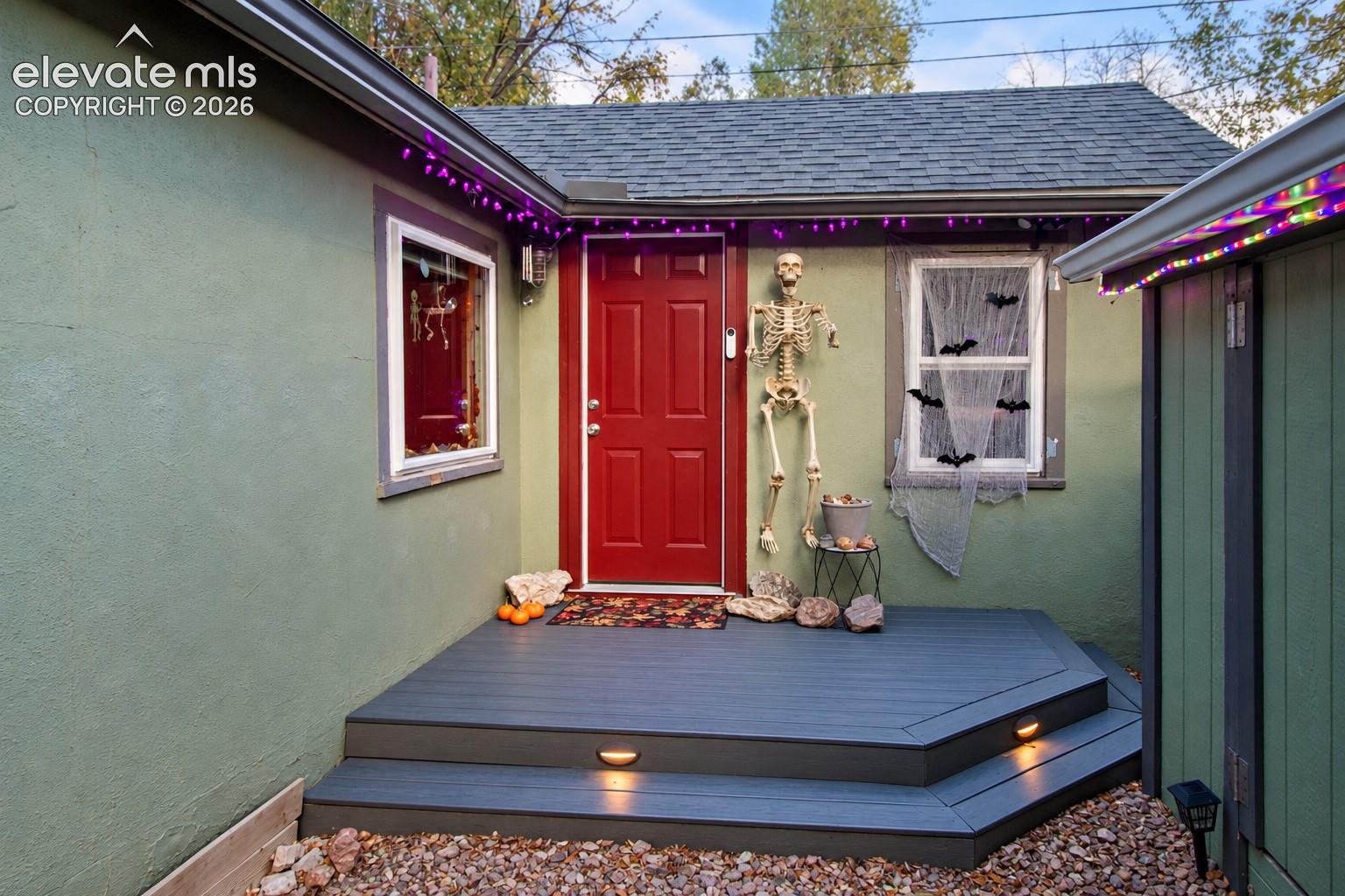 Exterior entry featuring a multi-level composite deck, integrated step lighting, a red six-panel entry door, and light-toned exterior siding