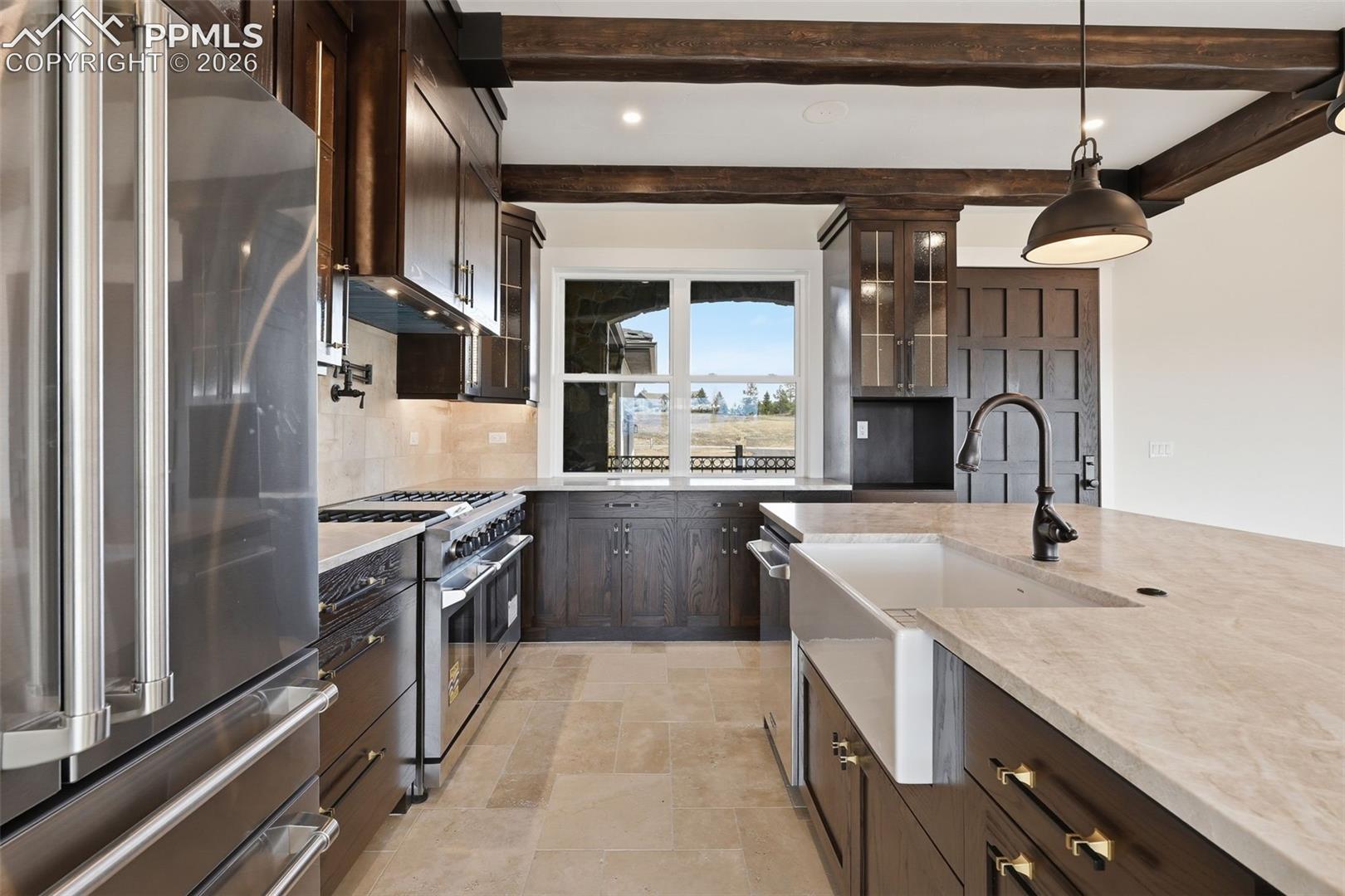 Kitchen with dark wood finish cabinets, high end appliances, glass insert cabinets, light stone finish floors, and decorative backsplash View is west to east.