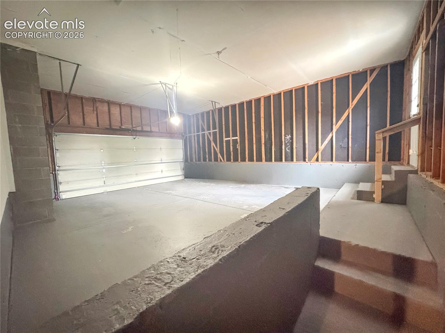 Multi-car garage featuring a sectional metal overhead door, concrete flooring, exposed wall studs, and tiered concrete steps