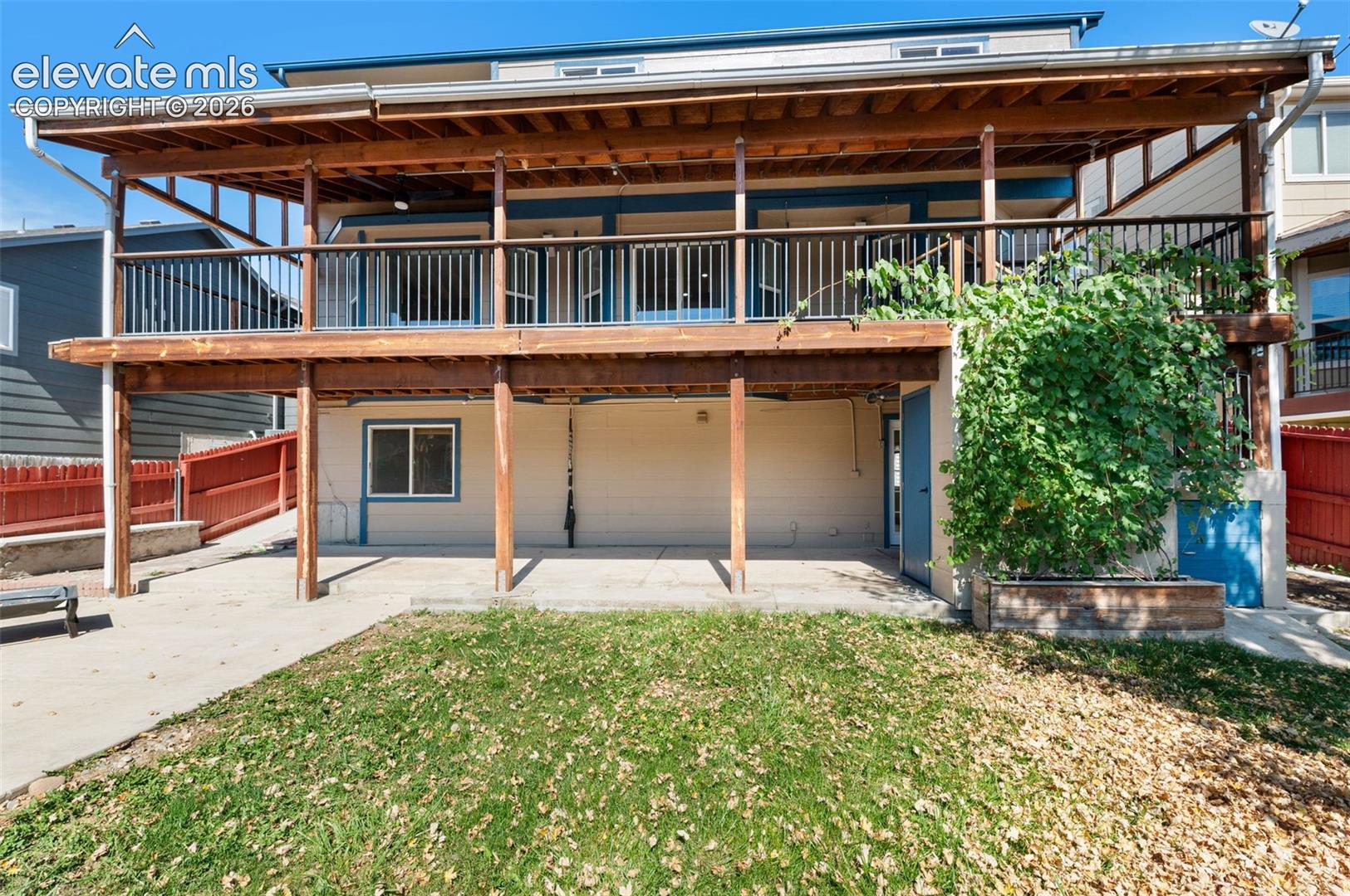 Two-story wood-finish deck with dark railings, concrete patio, and ground-level entry with a light-colored exterior finish