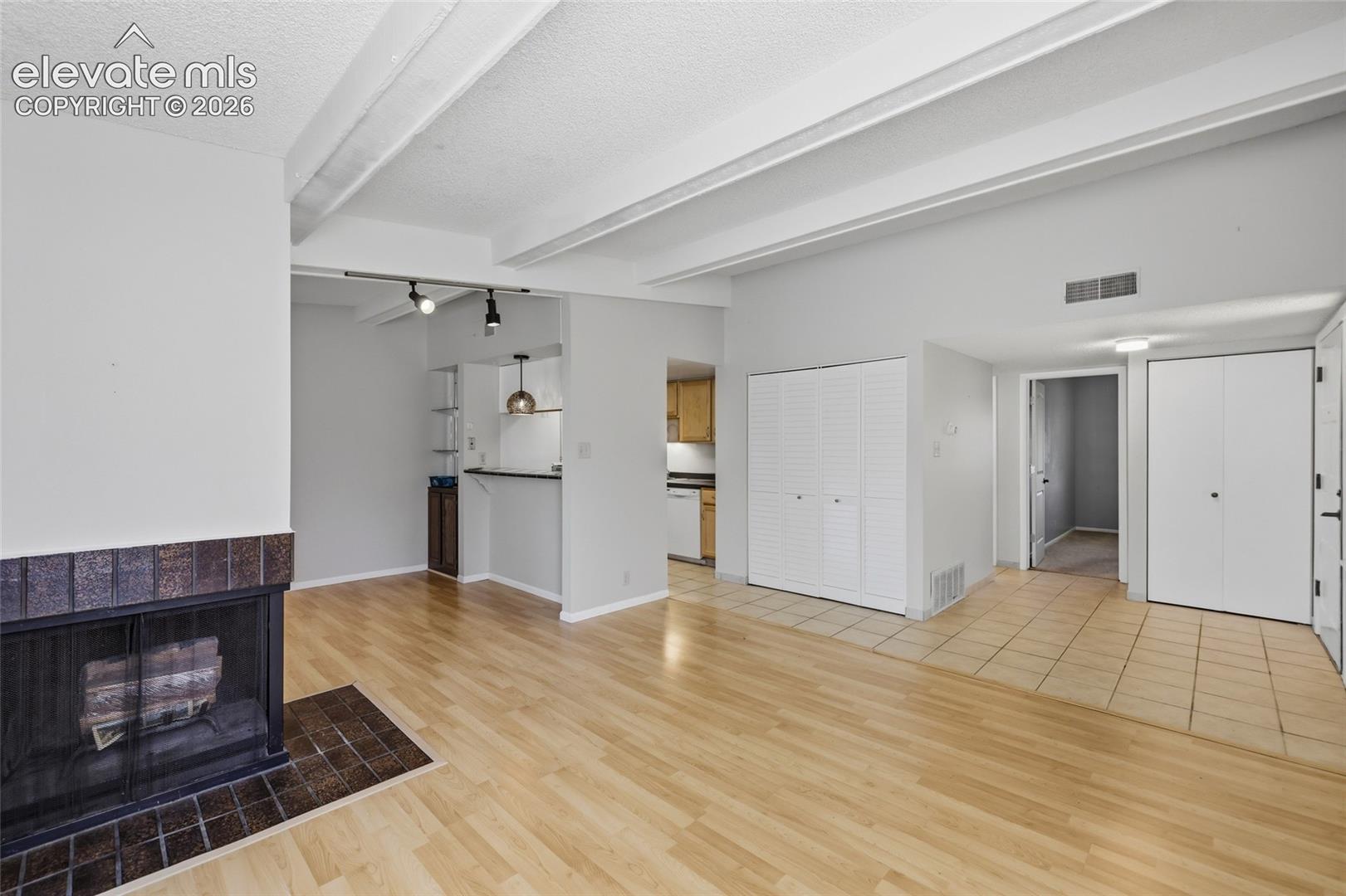 Living area featuring vaulted ceilings with exposed beams, wood-finish flooring, a tile-surround wood fireplace, and an integrated breakfast bar