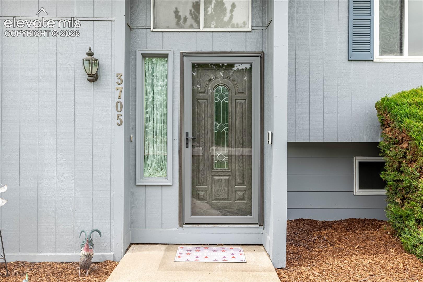 Exterior entry featuring vertical wood siding, a recessed front door with an arched glass insert, a narrow sidelight window, and a transom window