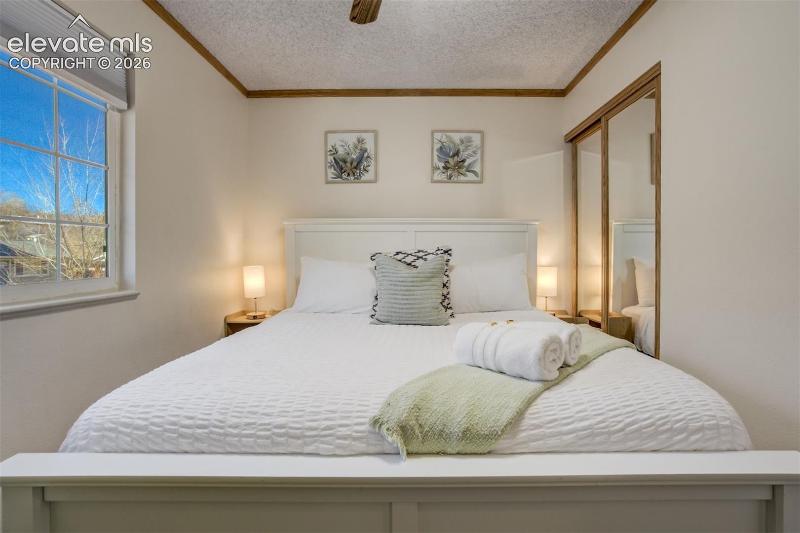 White paneled headboard and footboard, double-pane window, wall-mounted light fixtures, mirrored sliding closet doors, and wood-finish trim