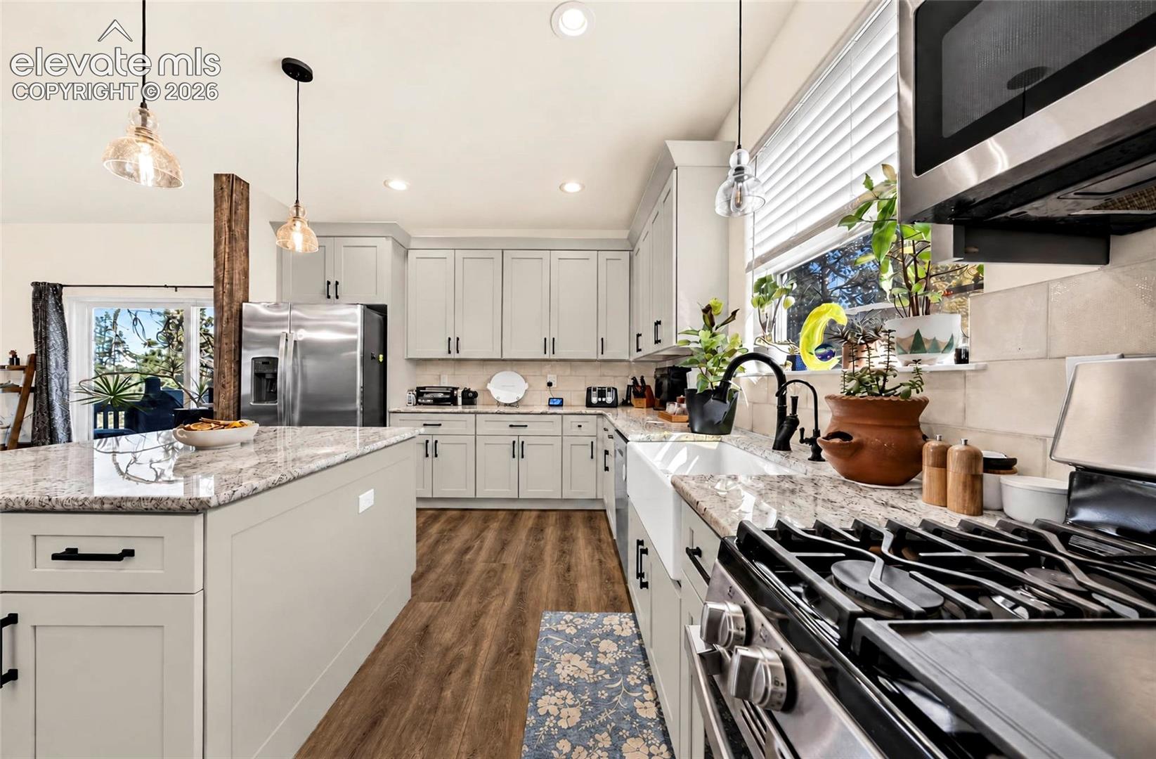 Kitchen featuring light-toned shaker-style cabinetry, stone countertops, a farmhouse-style apron sink with a matte black faucet, wood-finish flooring, and a central island