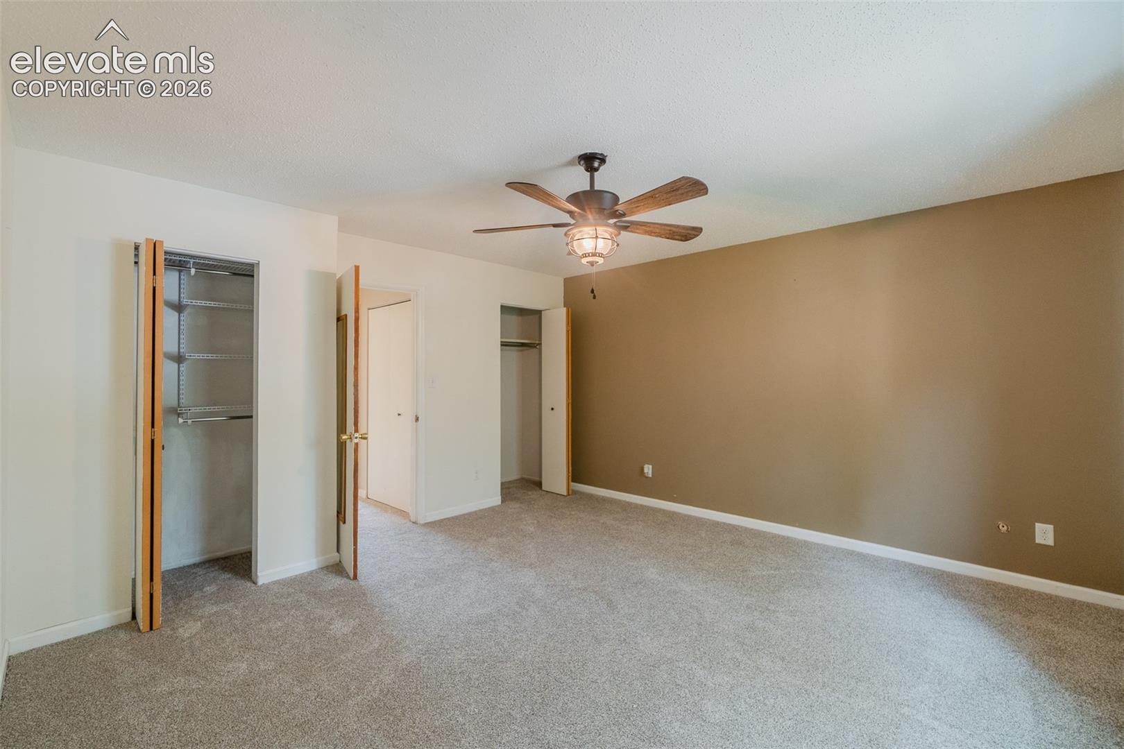 Neutral tone wall, textured ceiling, ceiling fan with integrated lighting, two built-in closets with bi-fold doors, and carpeting