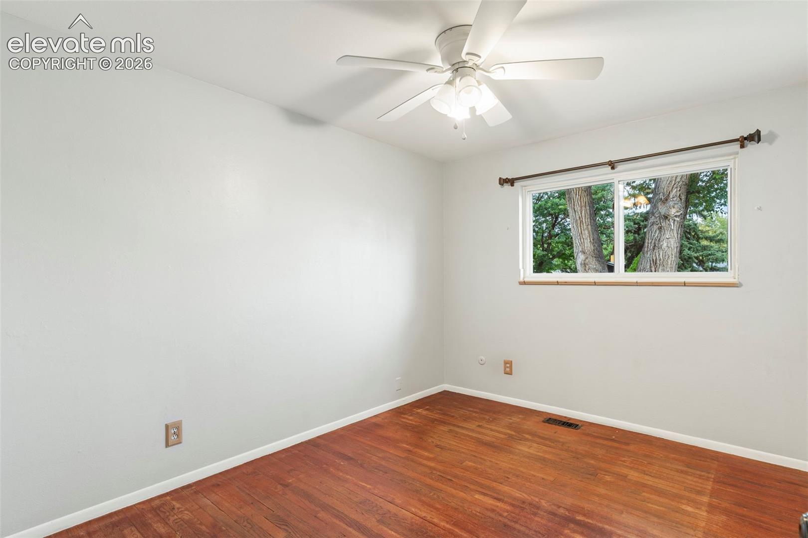 Hardwood flooring, white painted walls, white ceiling fan, and a window with a curtain rod
