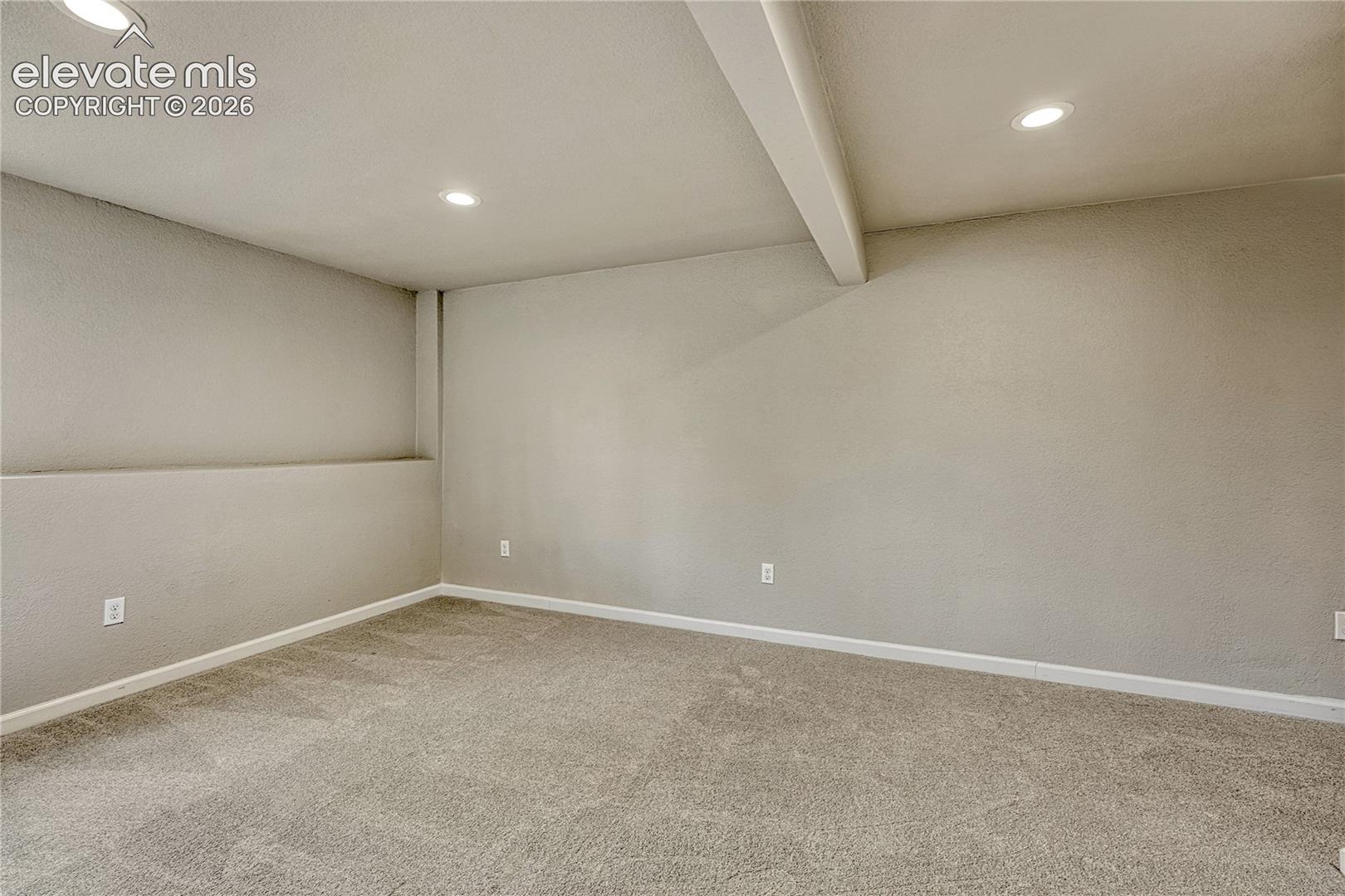 Interior space featuring neutral wall-to-wall carpeting, smooth-finish walls, recessed ceiling lighting, and a structural ceiling beam