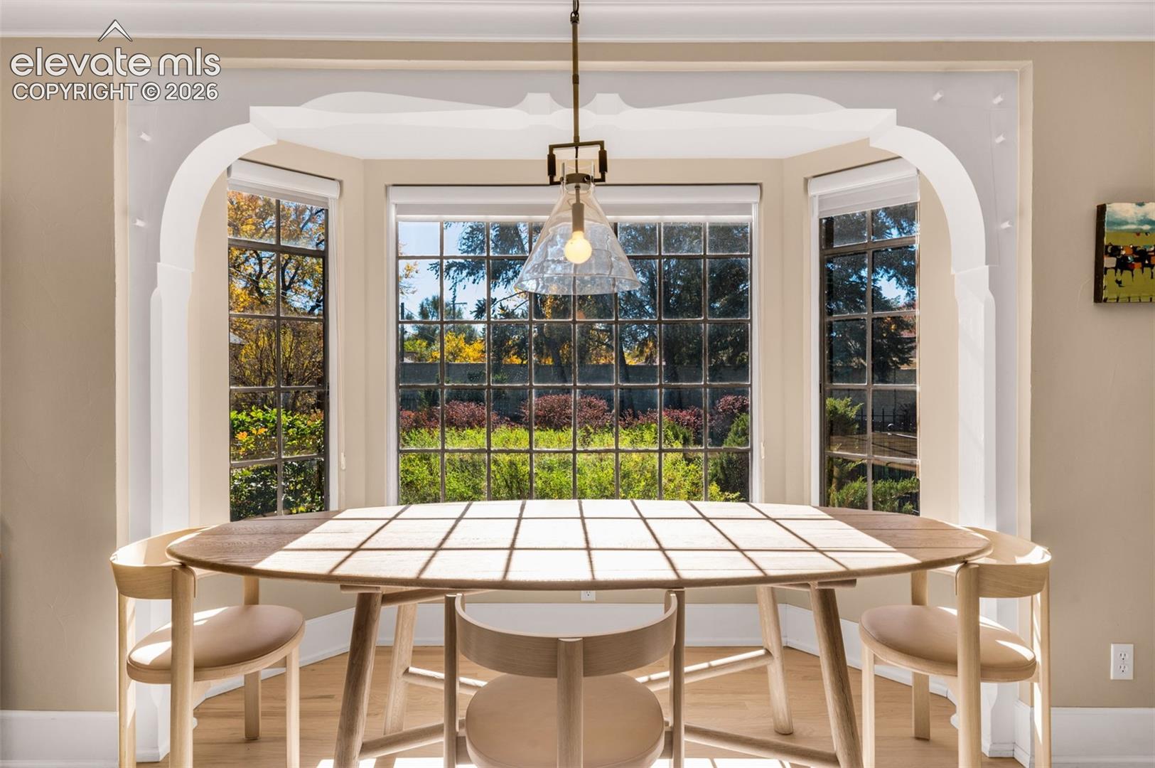 Bay window with multi-pane glazing, decorative millwork arch, pendant lighting fixture, and light-toned wood-finish flooring