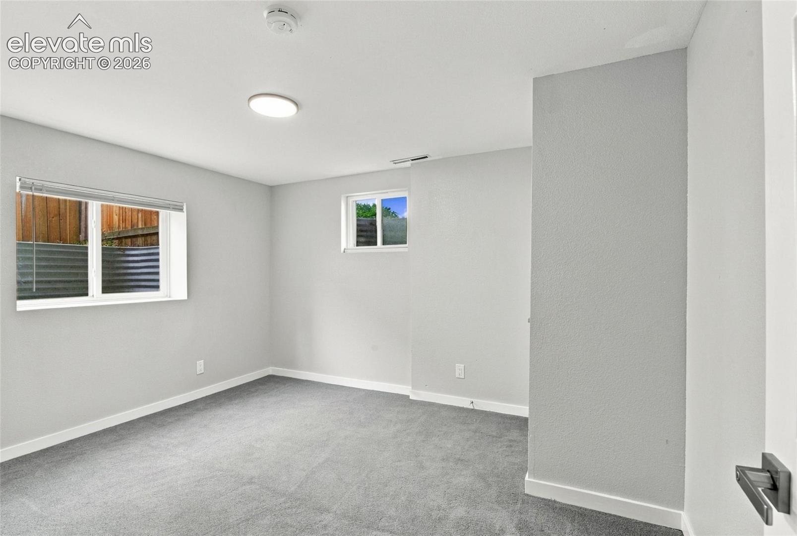 Neutral-toned interior space featuring wall-to-wall carpeting, light-colored wall finishes, and dual windows with window blinds