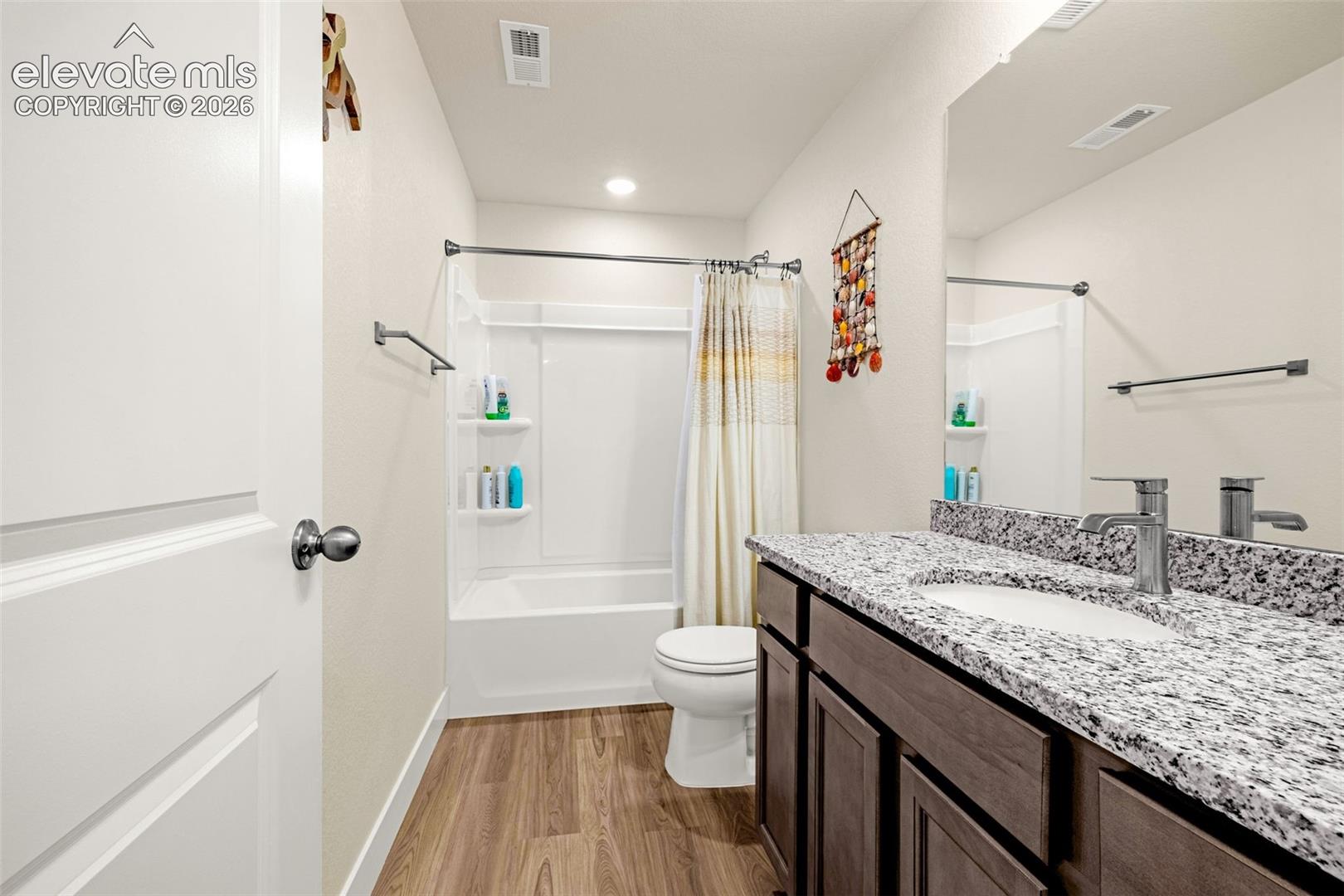 Bathroom featuring wood-finish flooring, a white tub-shower combination, a toilet, a vanity with a white countertop, and a large mirror