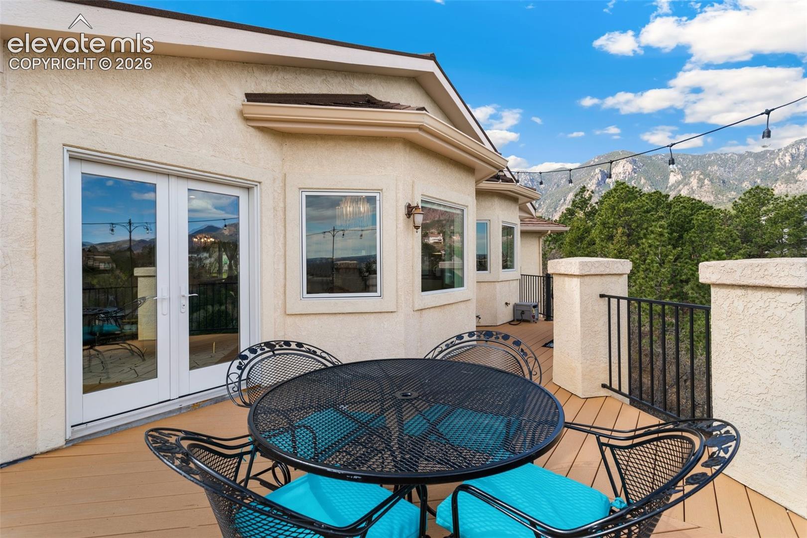 Exterior deck featuring a mountain backdrop, stucco finish, multiple windows, double glass doors, and a wood-finish deck surface