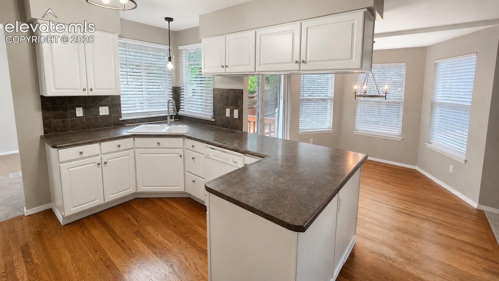 Kitchen featuring white cabinetry, dark countertops, a built-in sink, and wood-finish flooring