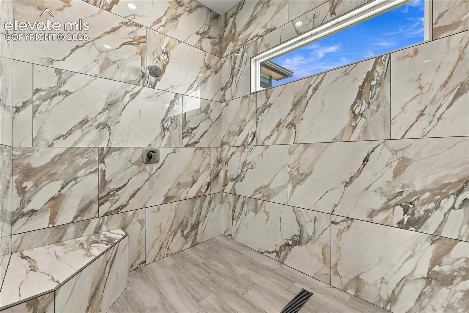 Shower enclosure featuring large-format veined tile walls, built-in tiled bench, horizontal clerestory window, and wood-finish tiled flooring with a linear drain