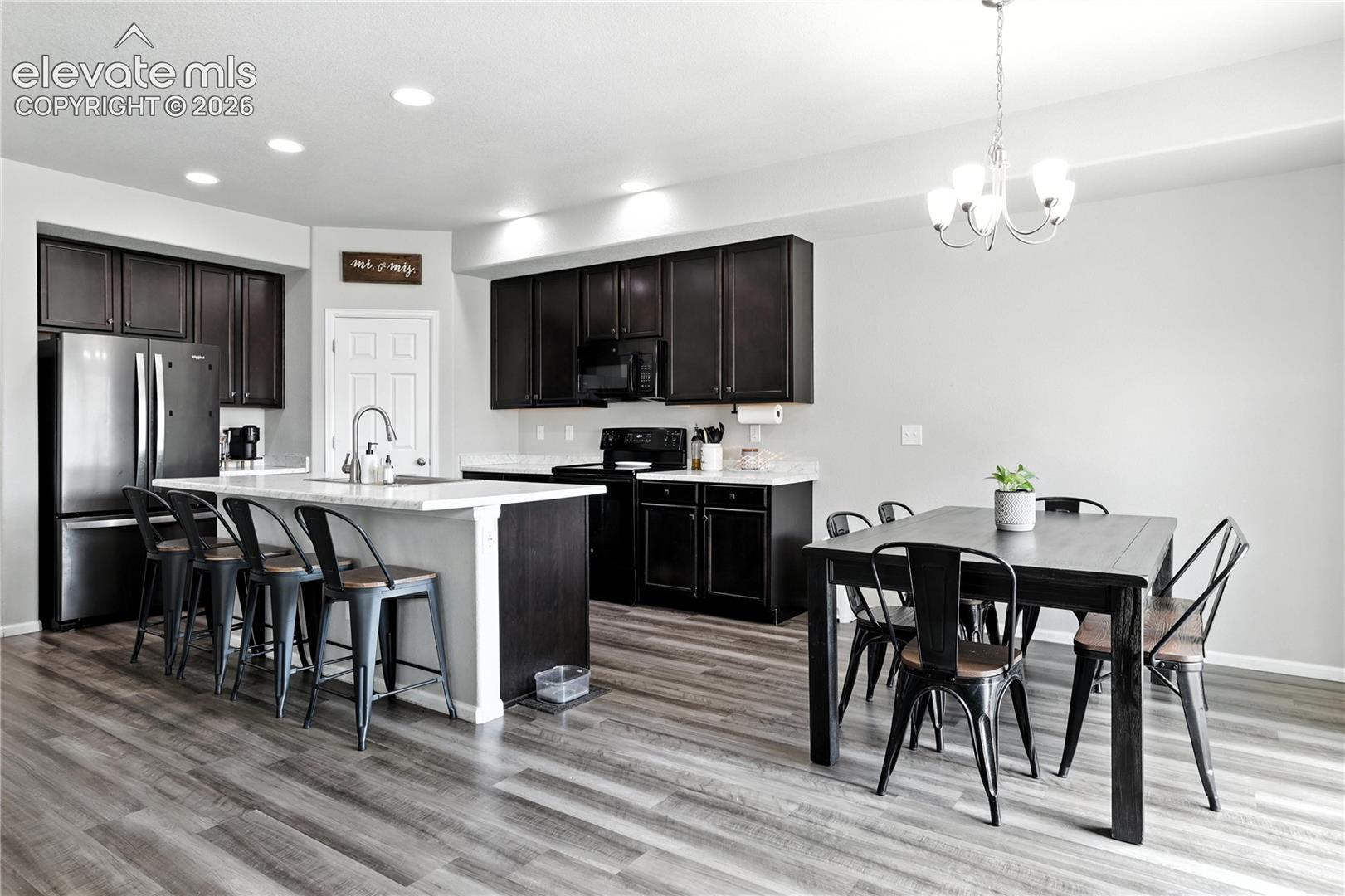 Kitchen featuring dark wood-finish cabinetry, stainless steel appliances, a center island with sink, and wood-finish flooring