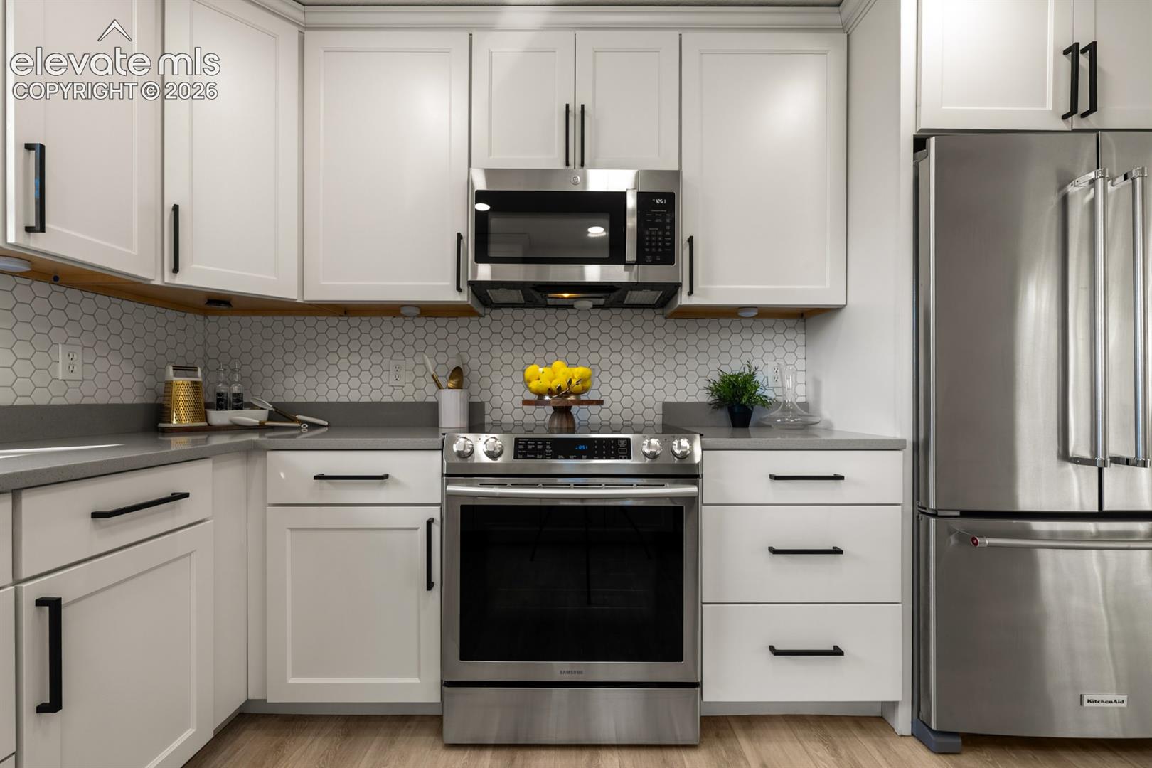 White shaker-style cabinetry with matte black hardware, stainless steel appliances, a honeycomb tile backsplash, and dark countertops