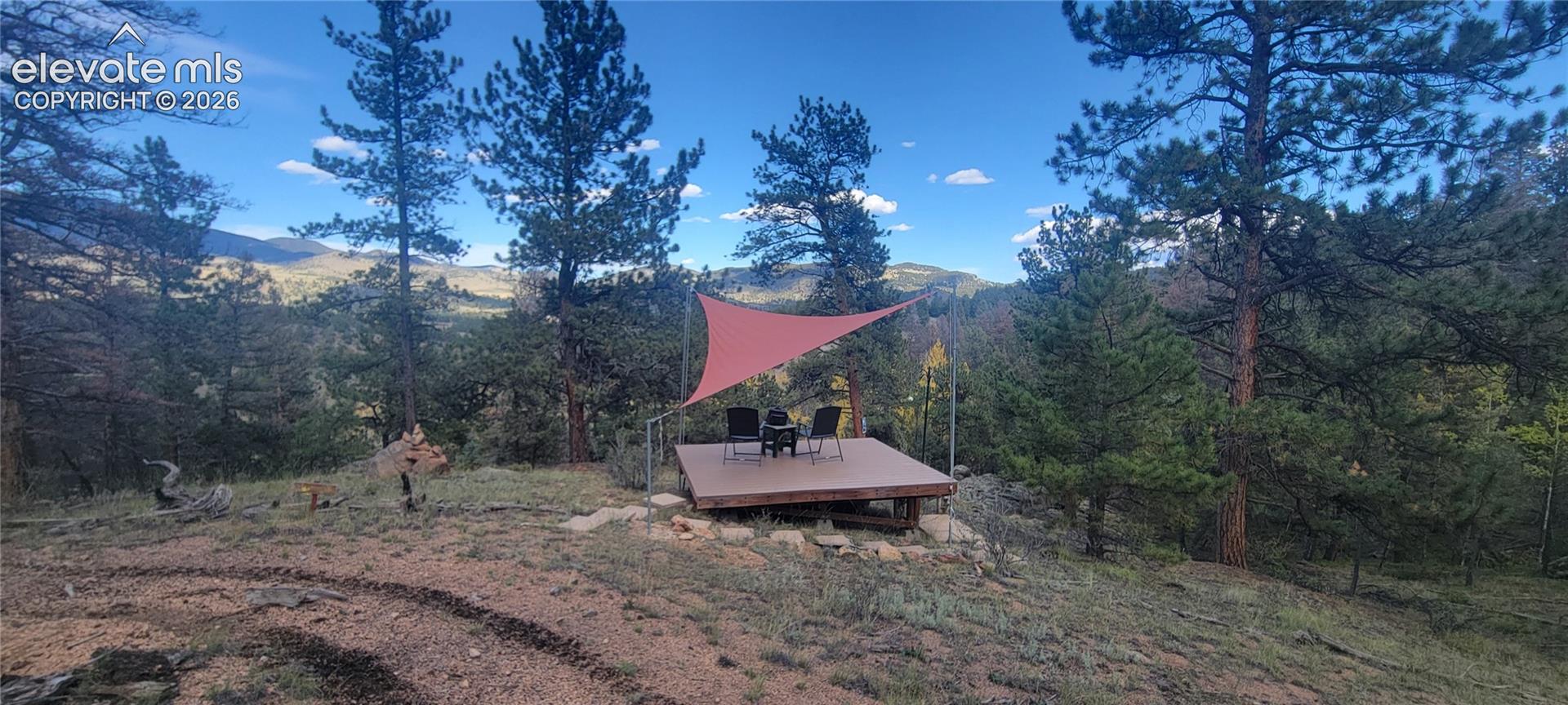 Elevated outdoor deck with a red shade sail, surrounded by mature evergreen trees