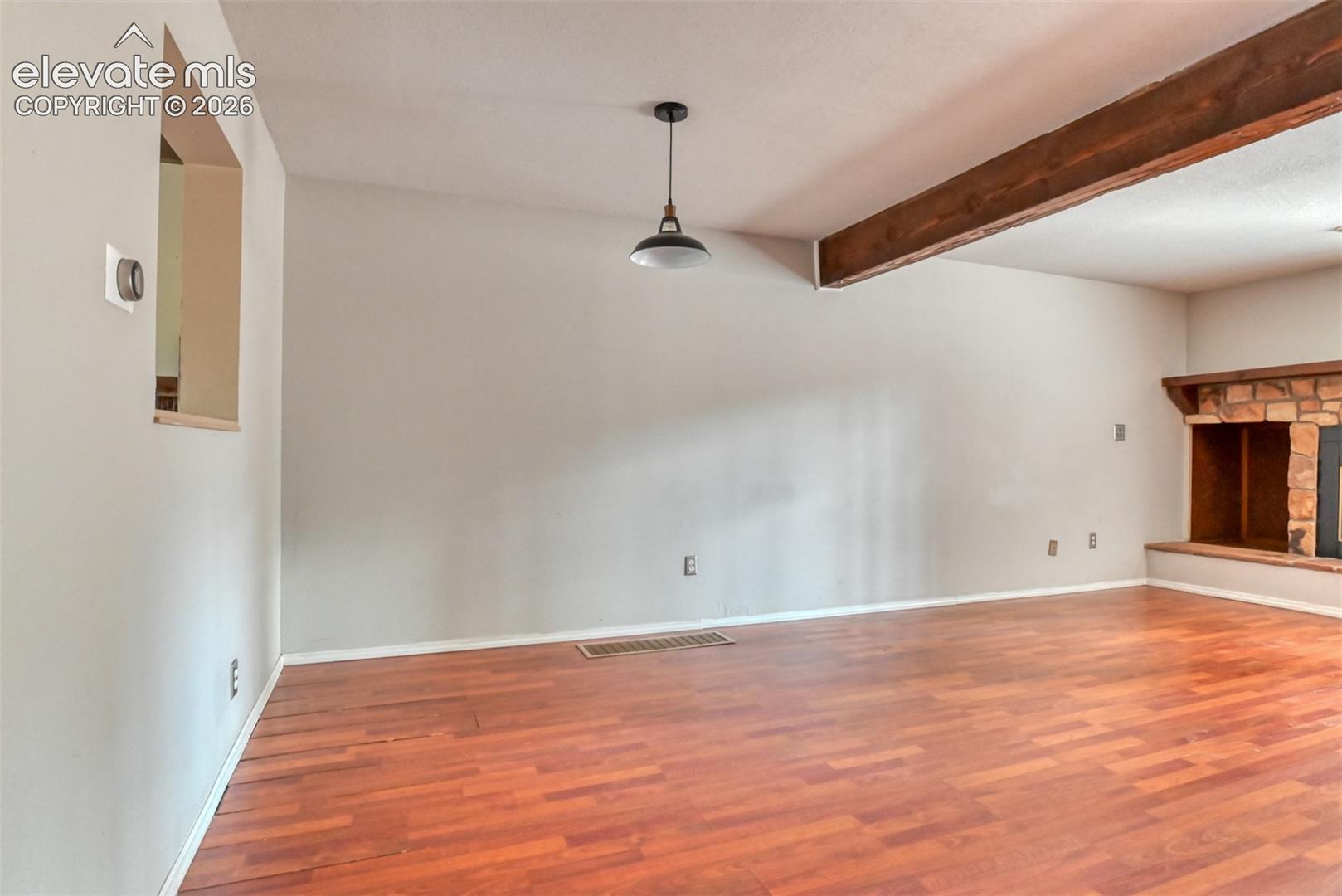 Wood-finish flooring with a stone fireplace, exposed ceiling beam, and suspended light fixture