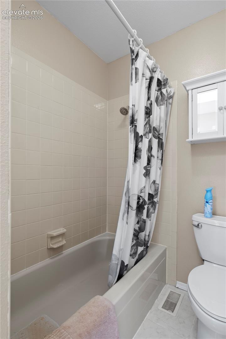 Recessed bathtub with surrounding tile, showerhead, and a wall-mounted storage cabinet