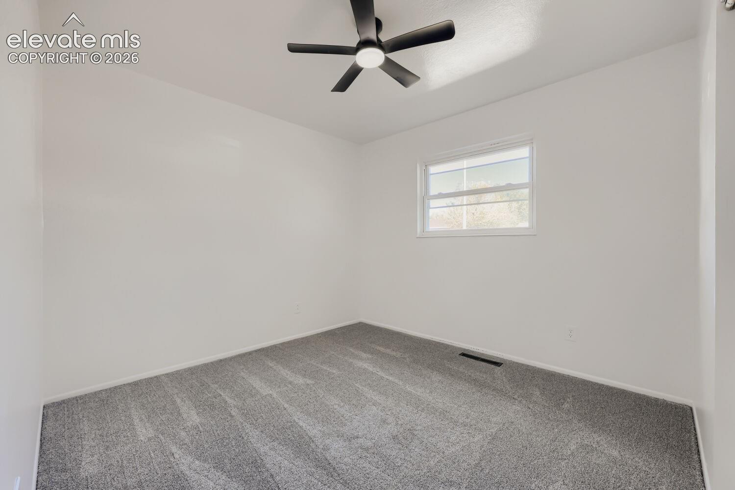 Neutral wall paint, gray patterned carpeting, window with white trim, and a black ceiling fan