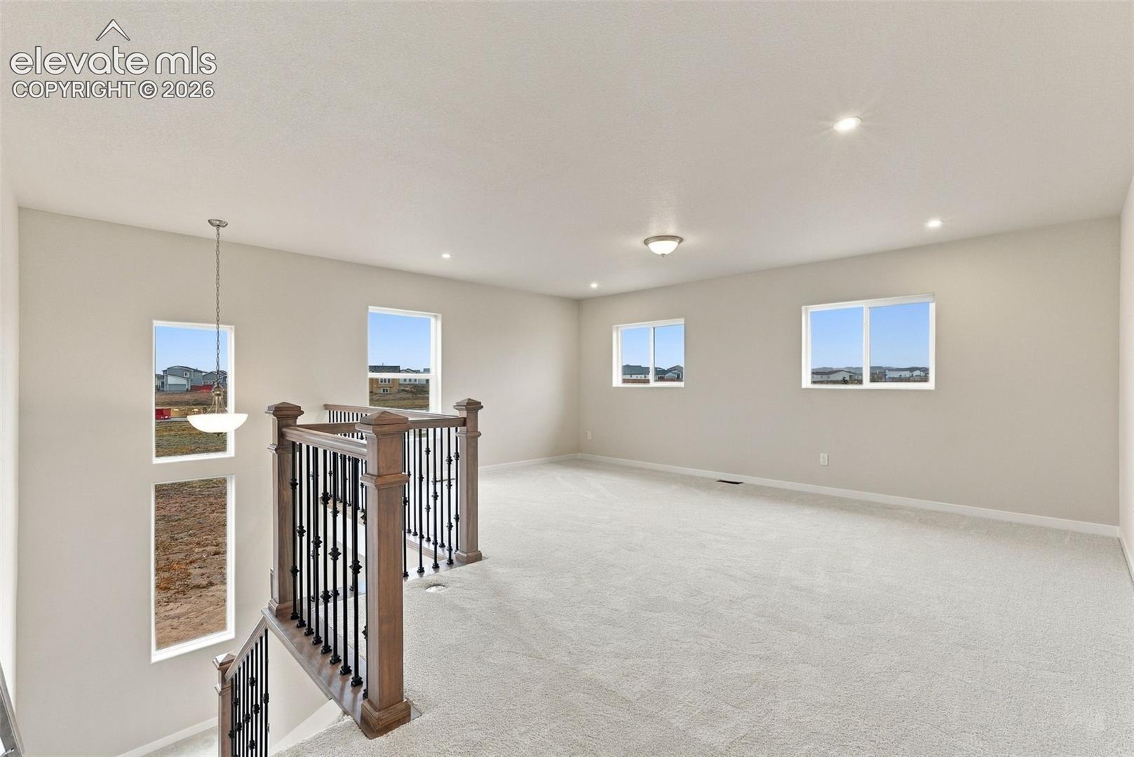 Open-concept interior featuring neutral wall tones, wall-to-wall carpeting, recessed lighting, and a staircase with a stained wood handrail and iron balusters